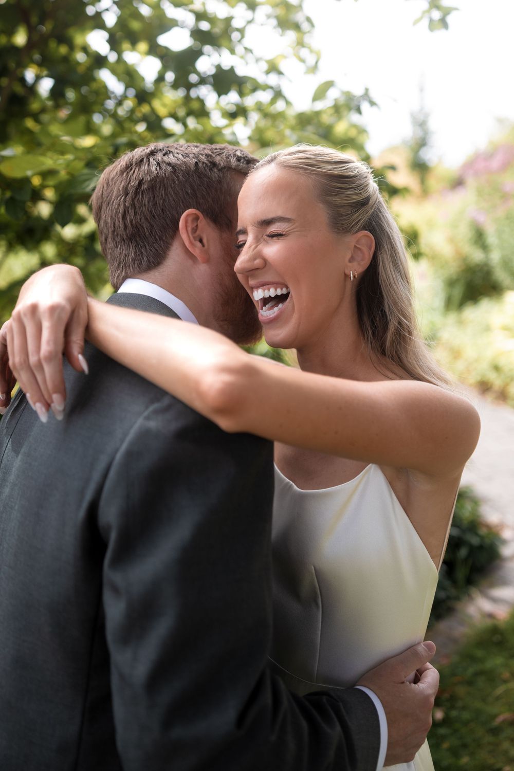 A romantic embrace between newlyweds in a garden setting, capturing a candid moment of laughter and joy.