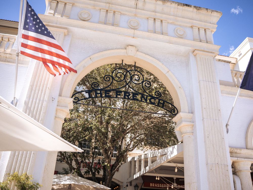 White Greek revival columns and American flags adorn the entrance of a historic government building on a sunny day.