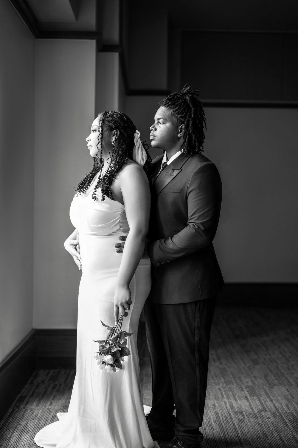 Black and white wedding portrait of a couple in formal attire standing together on a hardwood floor.