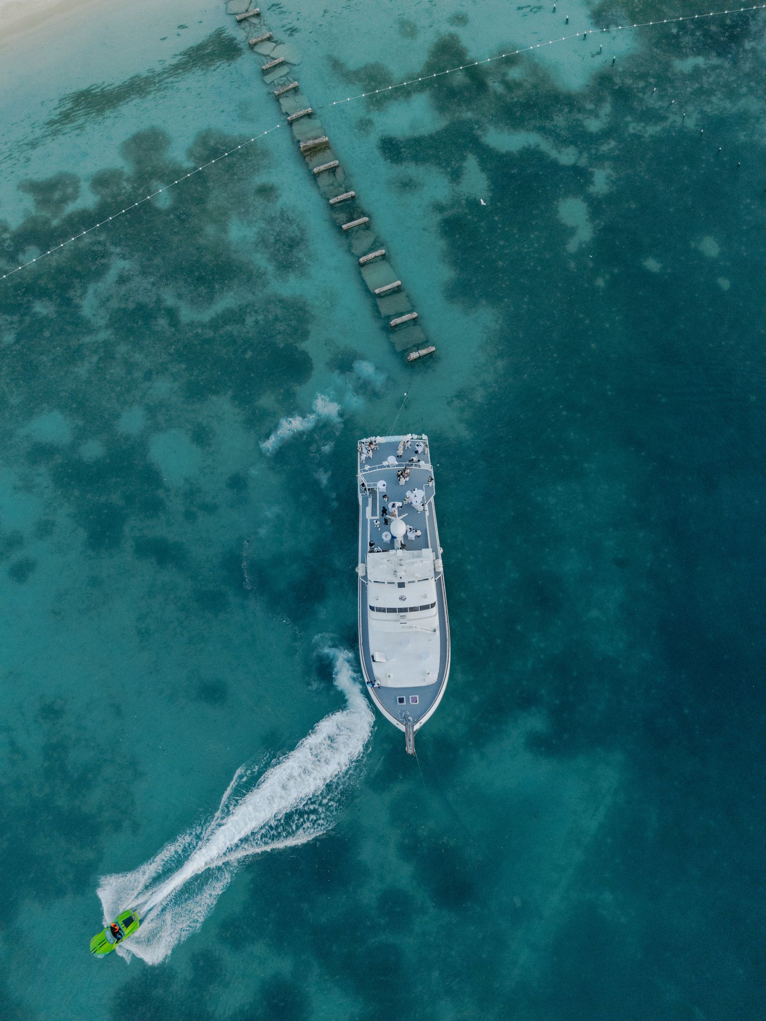 Aerial sequence of a white boat moving through crystal clear turquoise waters leaving a wake pattern behind.
