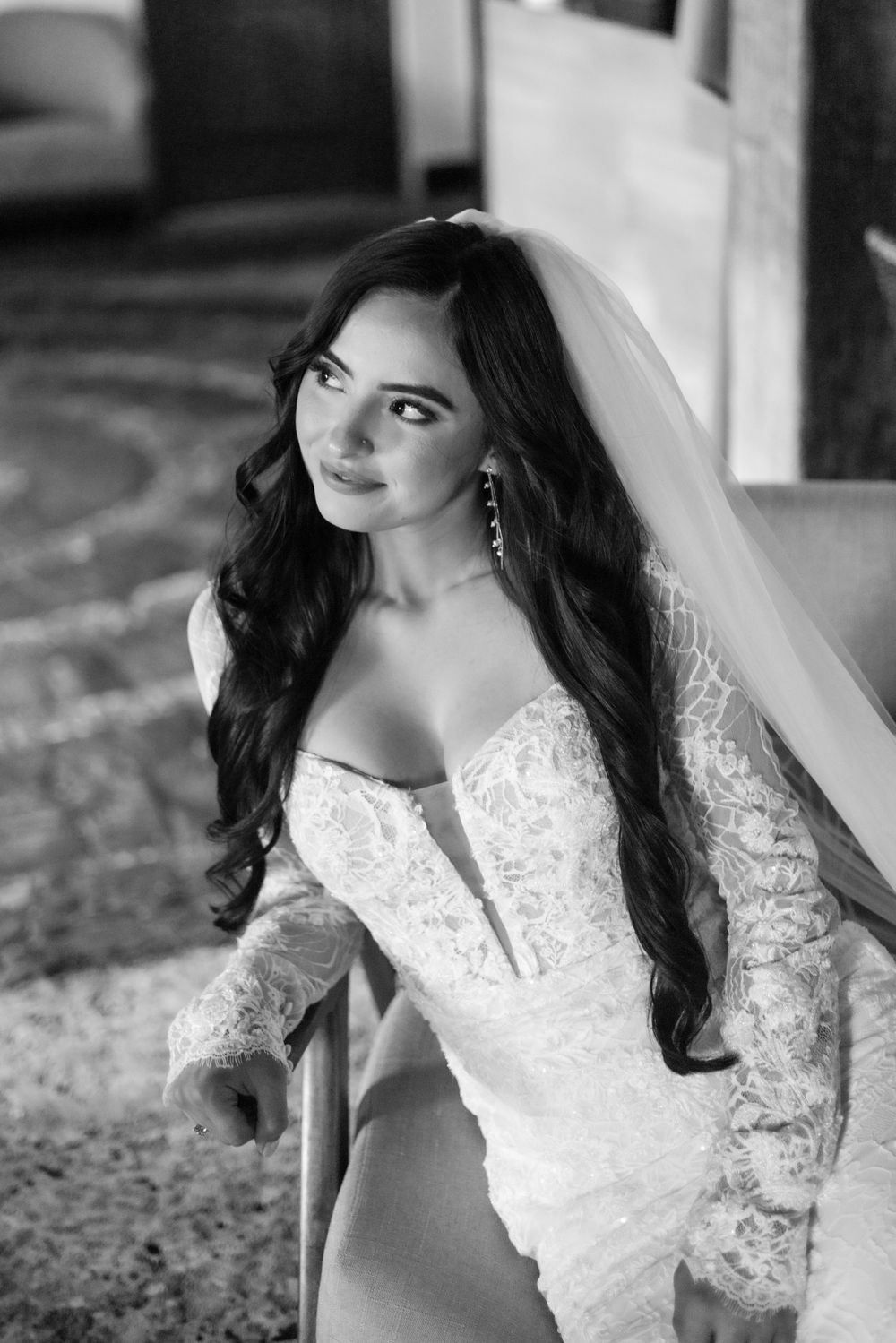 A bride in a white lace wedding dress with long sleeves and veil poses for a black and white portrait.