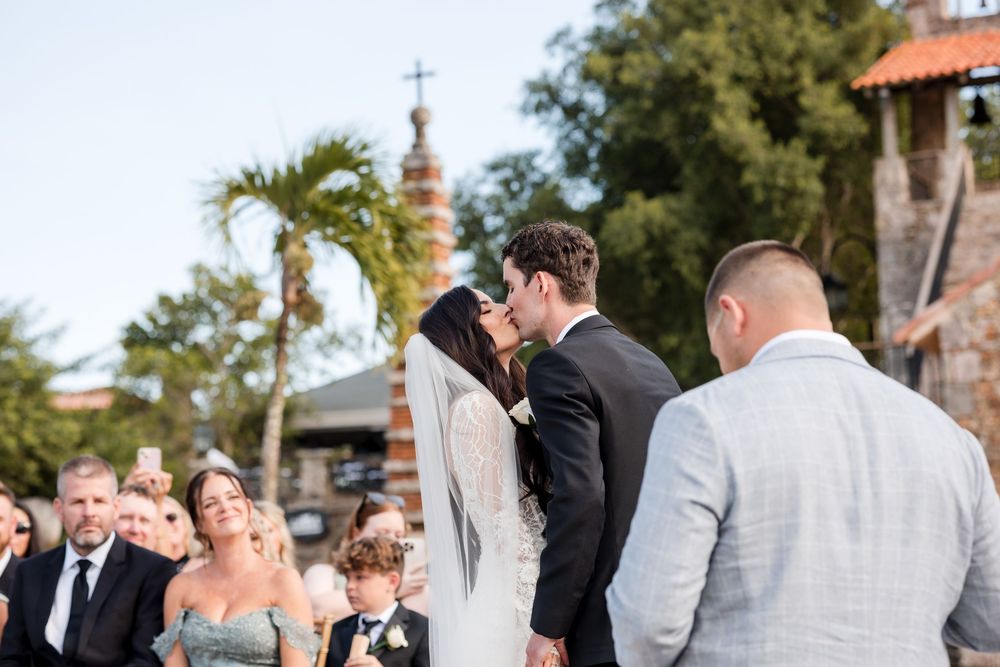 A group of wedding guests gather outdoors for a celebratory moment during a sunny afternoon ceremony.
