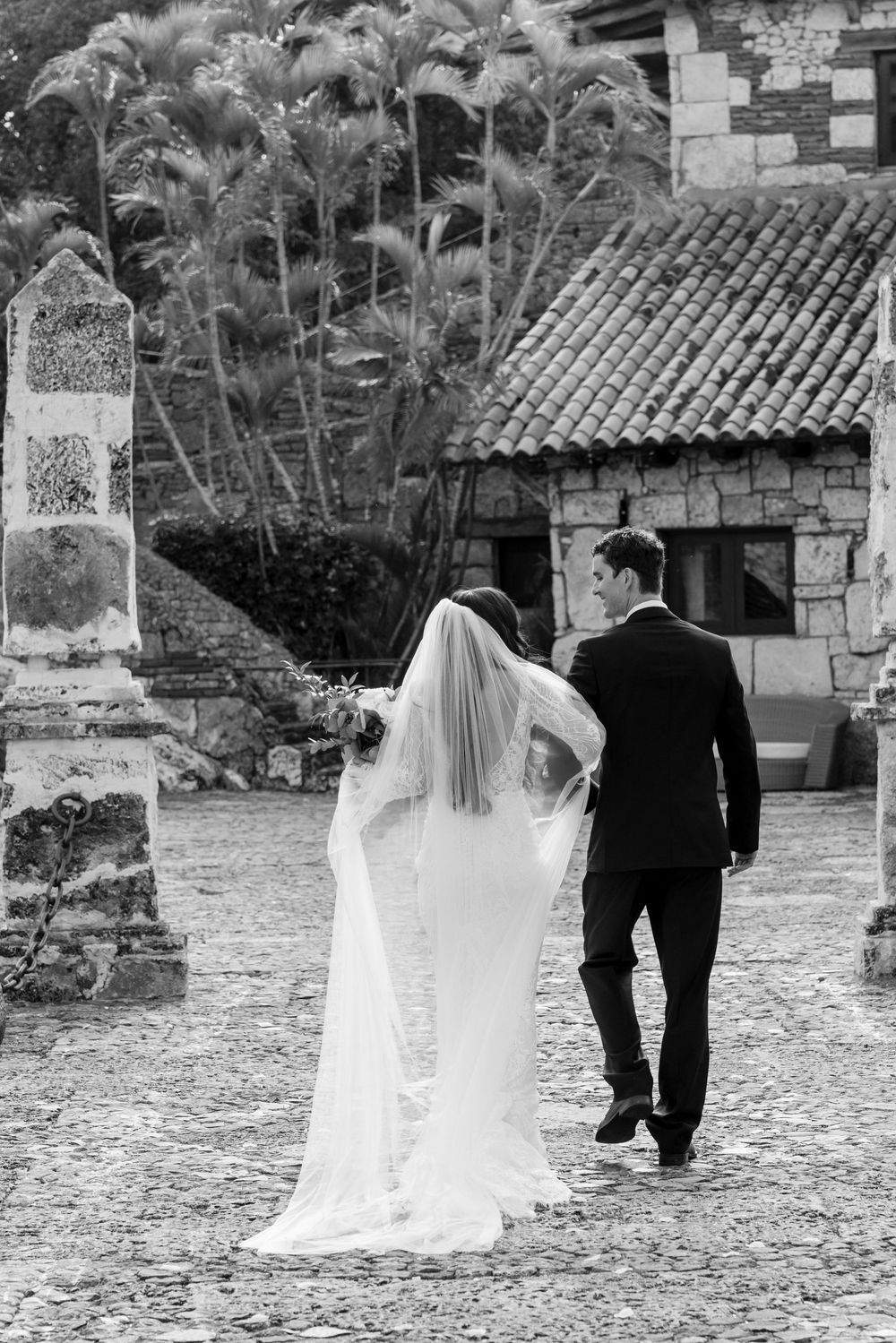 A sequence of black and white photos showing a couple walking away on a stone courtyard during their wedding day.