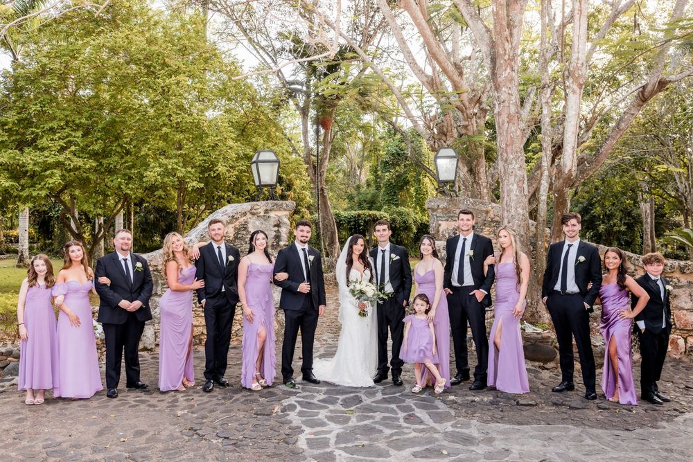 Wedding party in formal attire poses together outdoors with trees in the background during autumn.