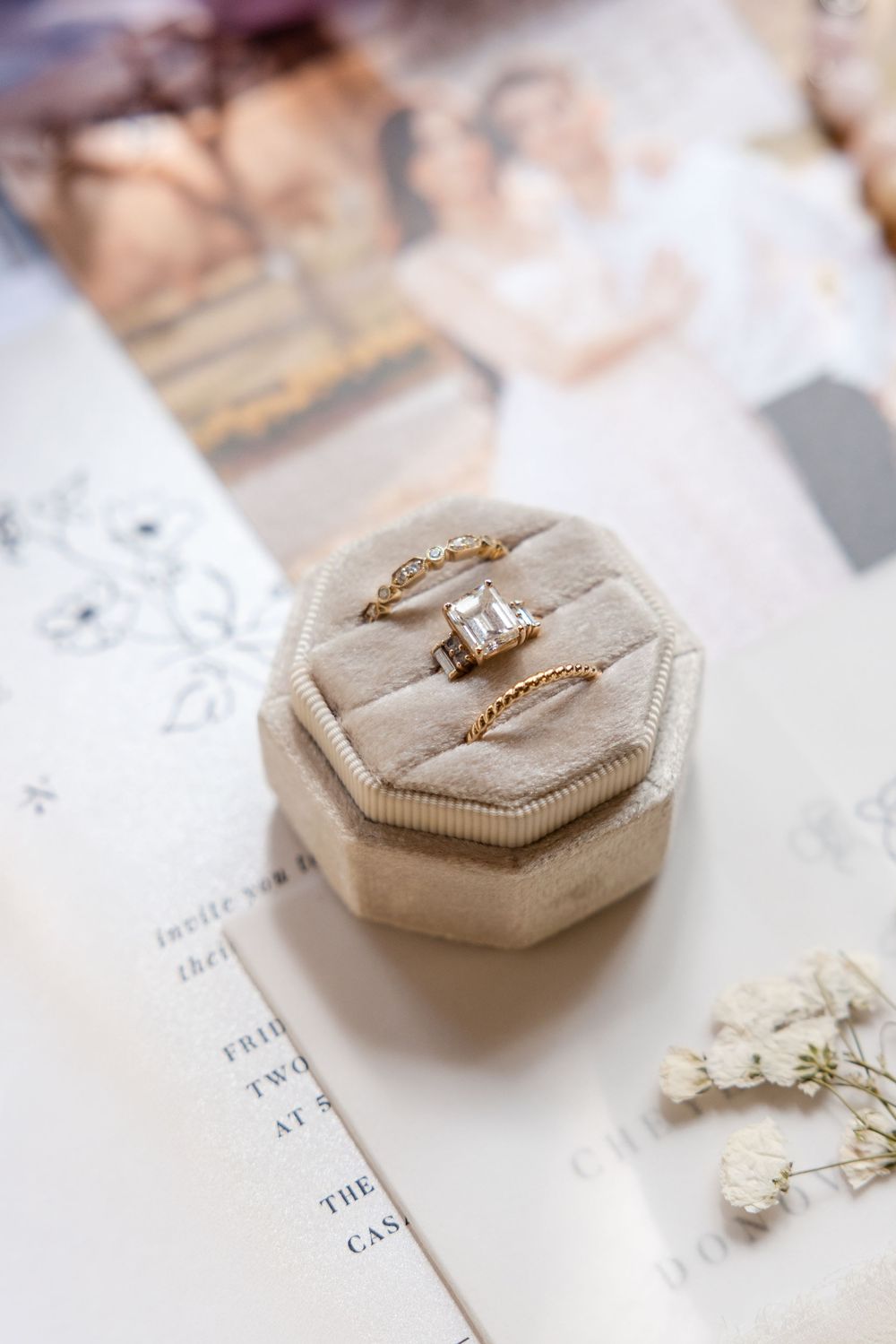 Gold wedding rings and engagement ring displayed on a beige hexagonal ring box against white paper.