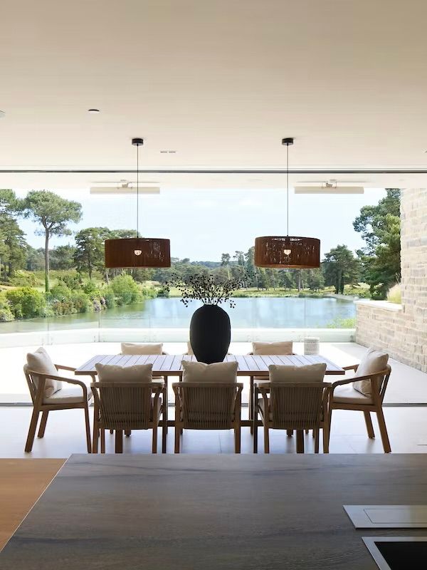 Modern dining area with sleek wooden chairs and panoramic windows overlooking a scenic countryside landscape.
