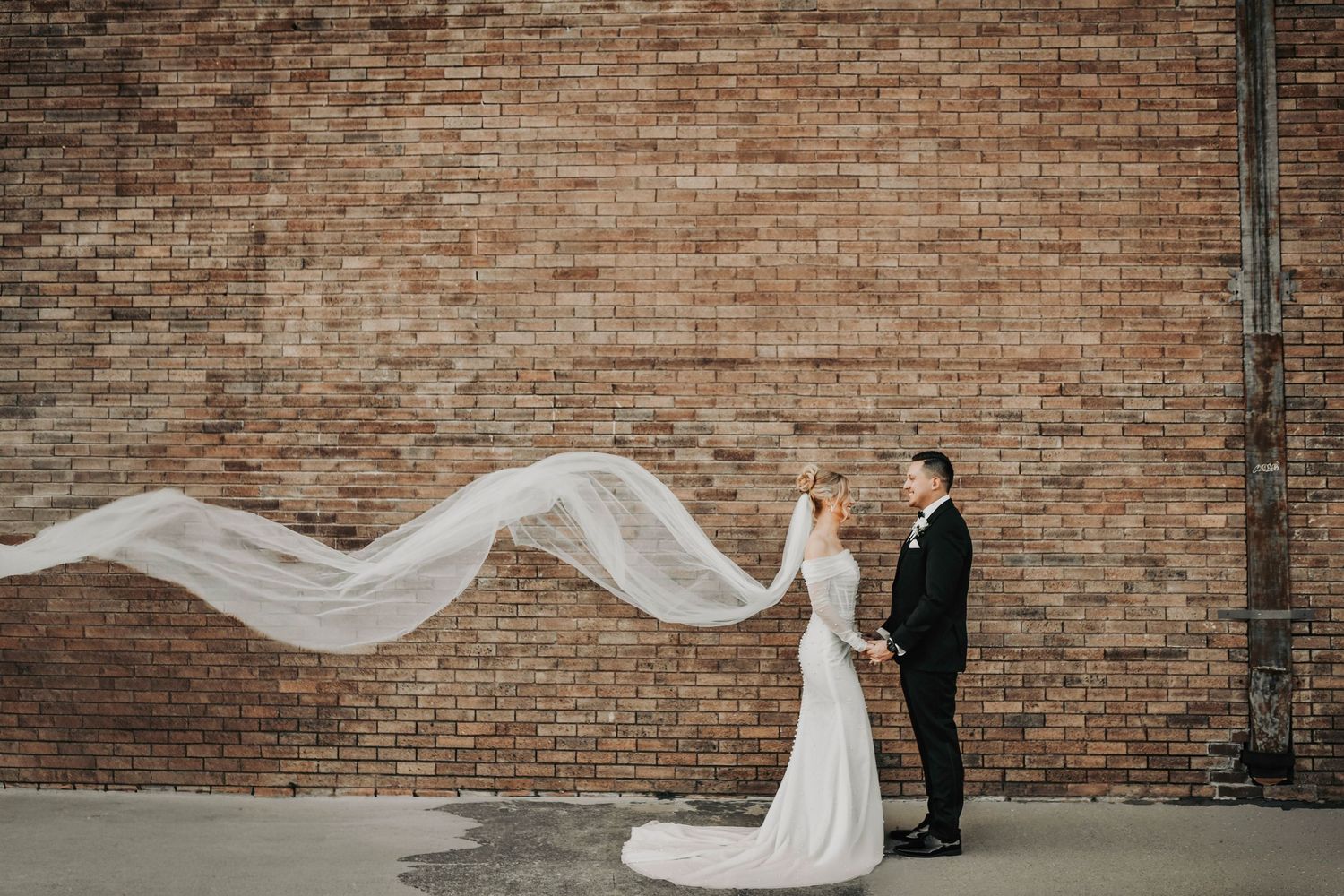 Editorial wedding photo of the couple standing against exposed brick in Deep Ellum, highlighted by sunset light and modern posing.
