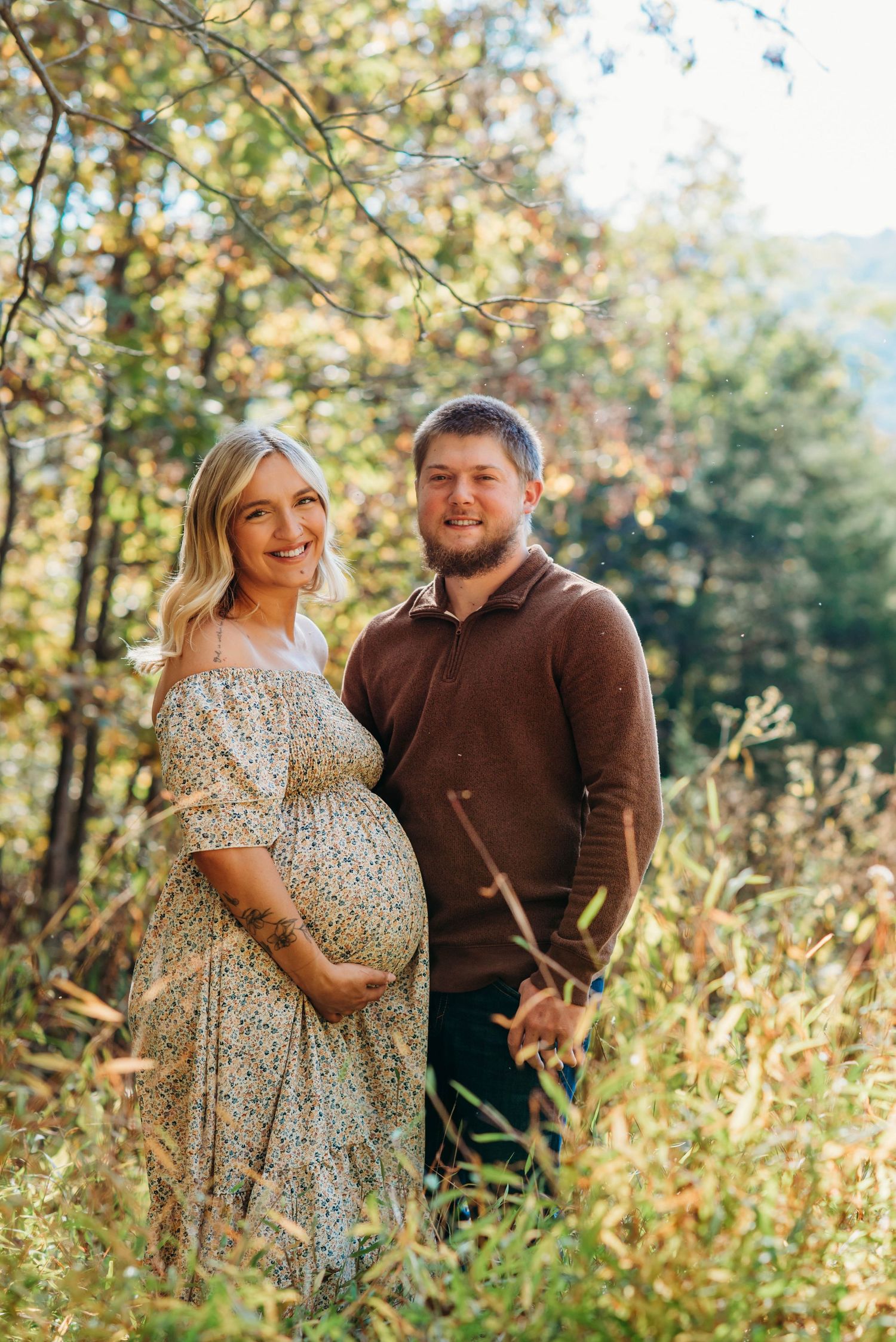 A couple shares joyful moments together in a sun-drenched autumn field with golden foliage in the background.