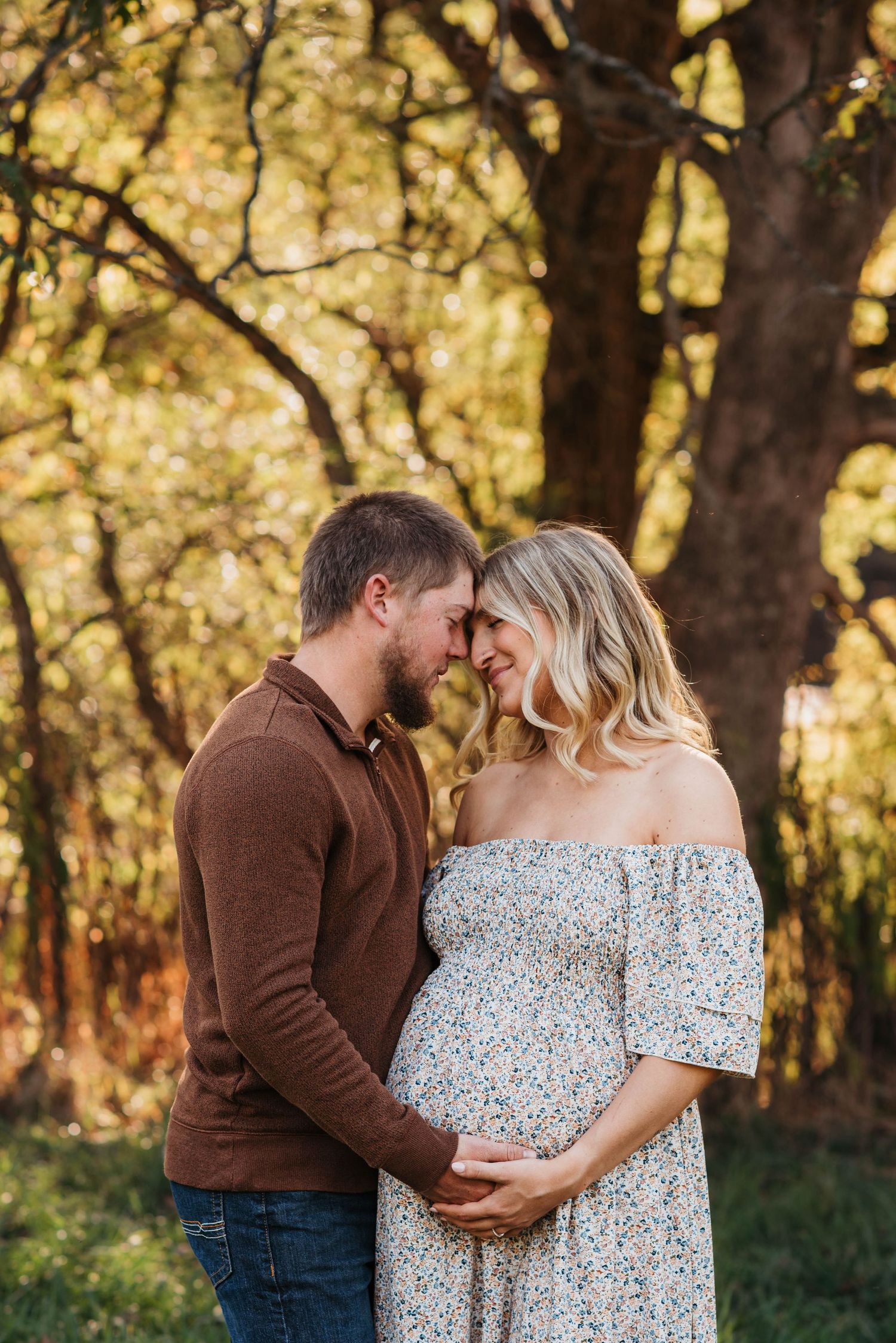 A romantic couple embraces in a sunlit autumn forest setting wearing brown and floral outfits.