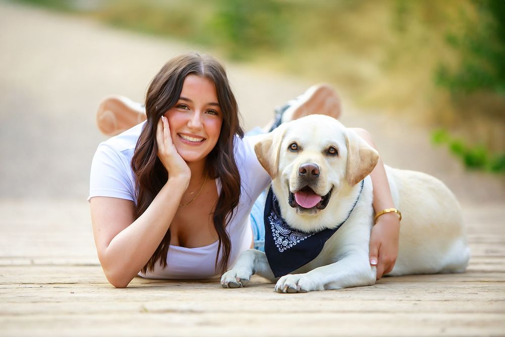 A white dog and person lying on a wooden deck enjoying a sunny day together.