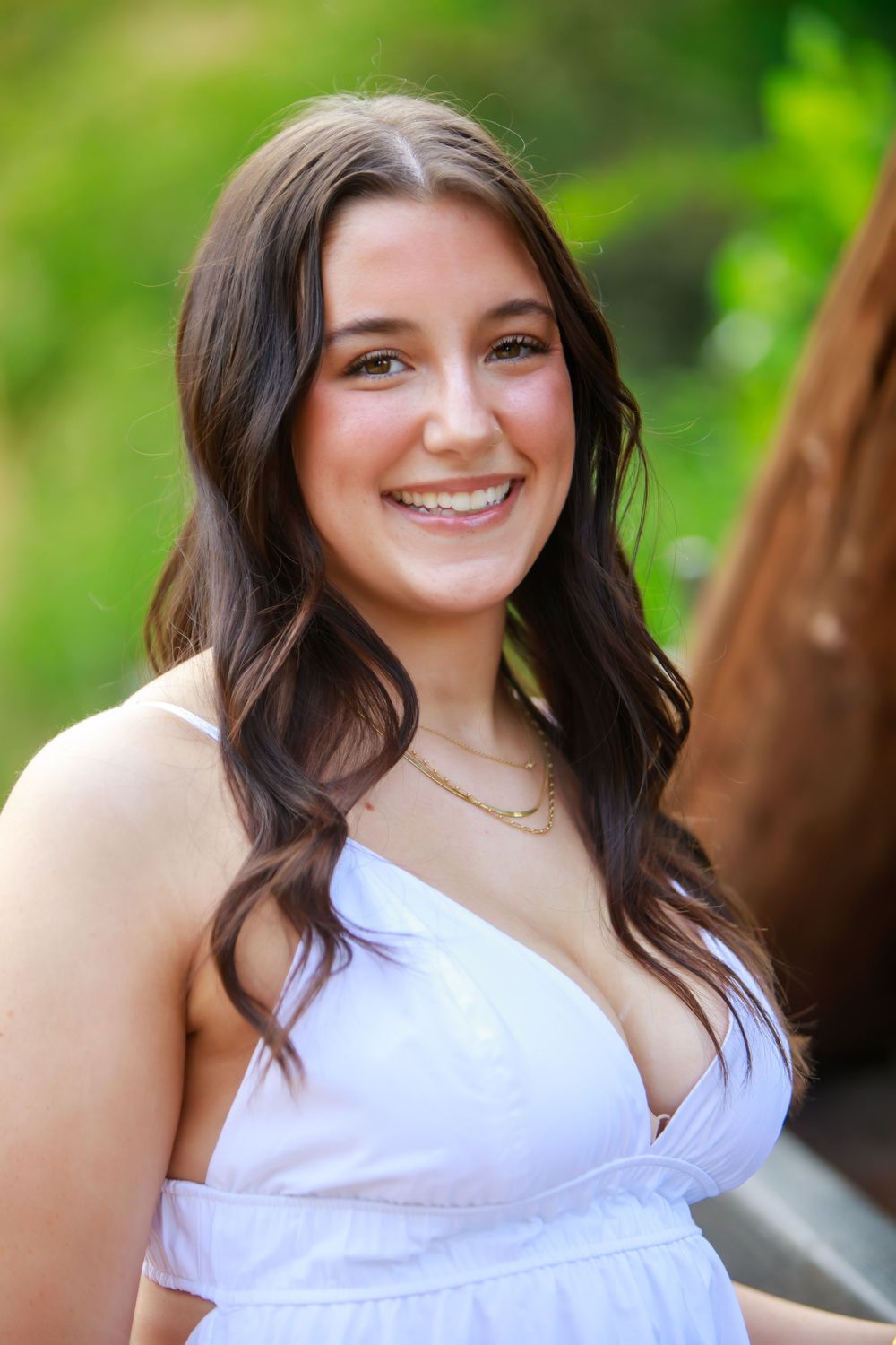 Portrait series in white top with natural green background showing warm expressions and wavy dark hair.