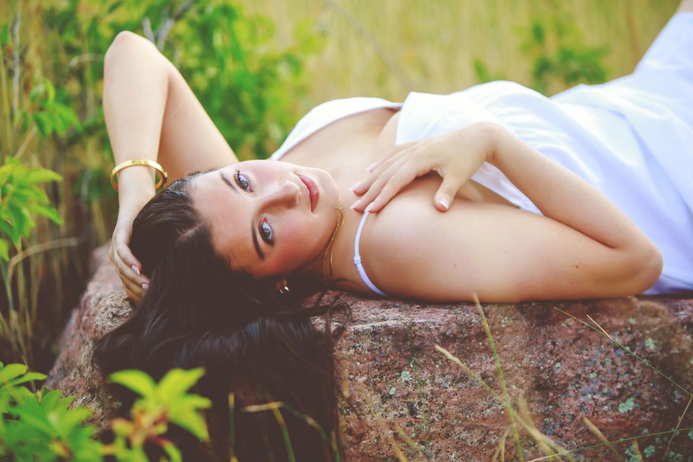 A person in white clothing poses gracefully on a fallen tree trunk in a lush green forest setting.