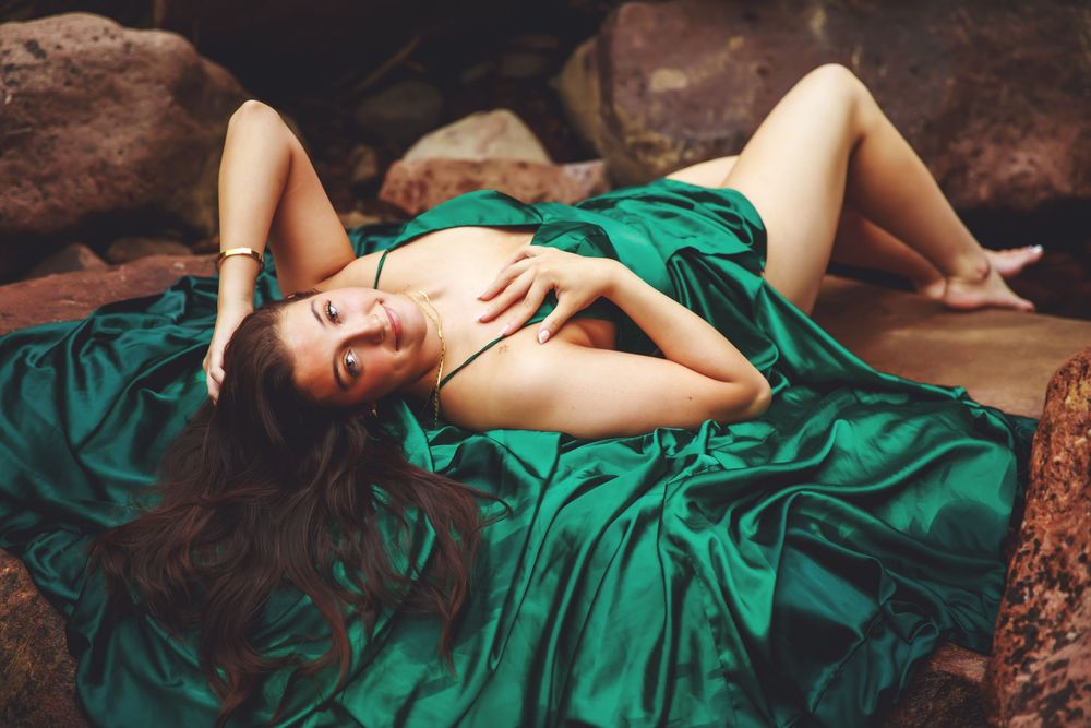 A person in an emerald green flowing dress lies gracefully on rocky terrain in an artistic outdoor portrait.