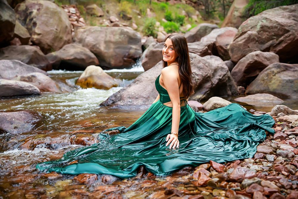 A flowing teal dress creates an ethereal scene against rocky creek waters in a nature-inspired photoshoot.
