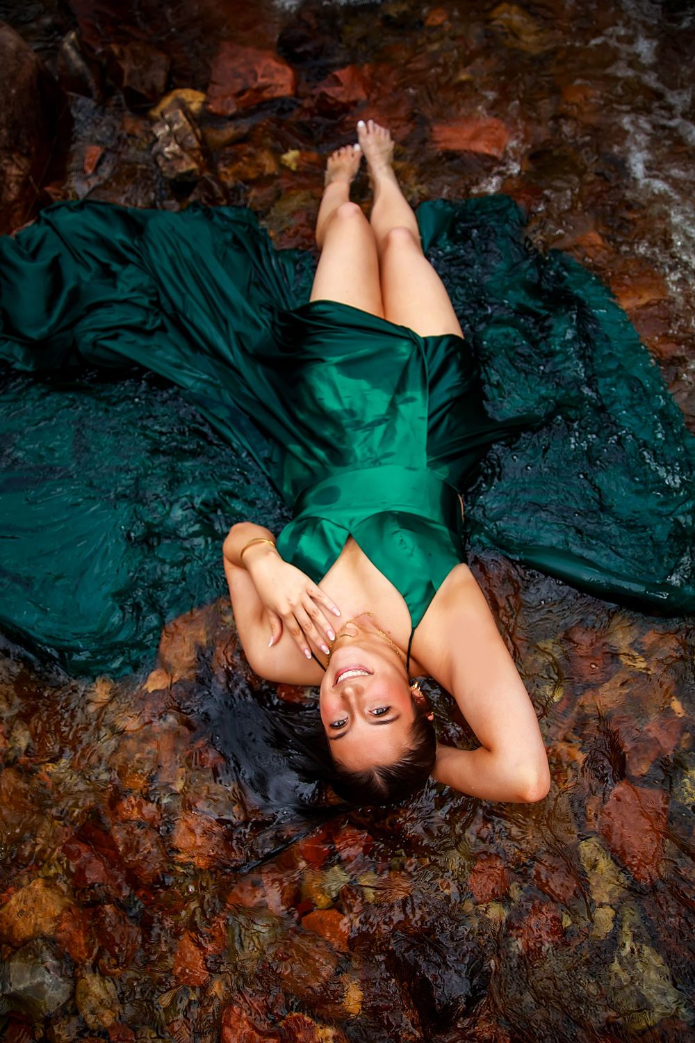 Person in emerald green dress poses dramatically on dark textured surface with artistic lighting and shadows.