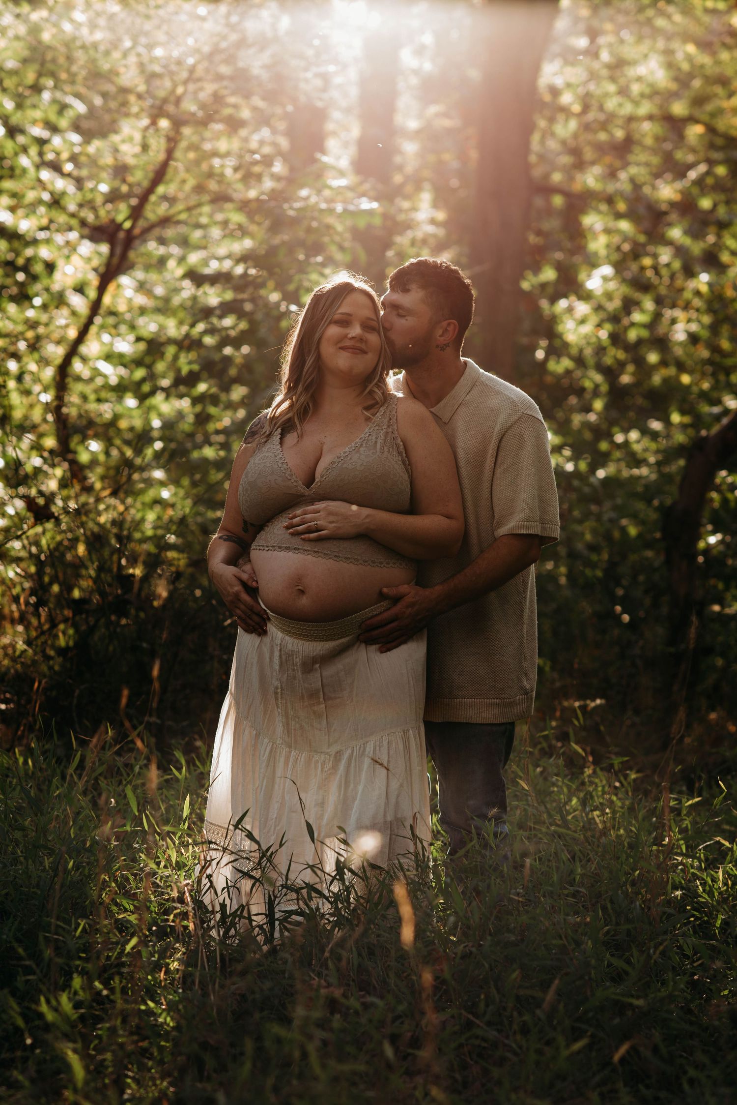 Intimate maternity photoshoot in a sunlit garden with golden hour lighting and natural foliage.