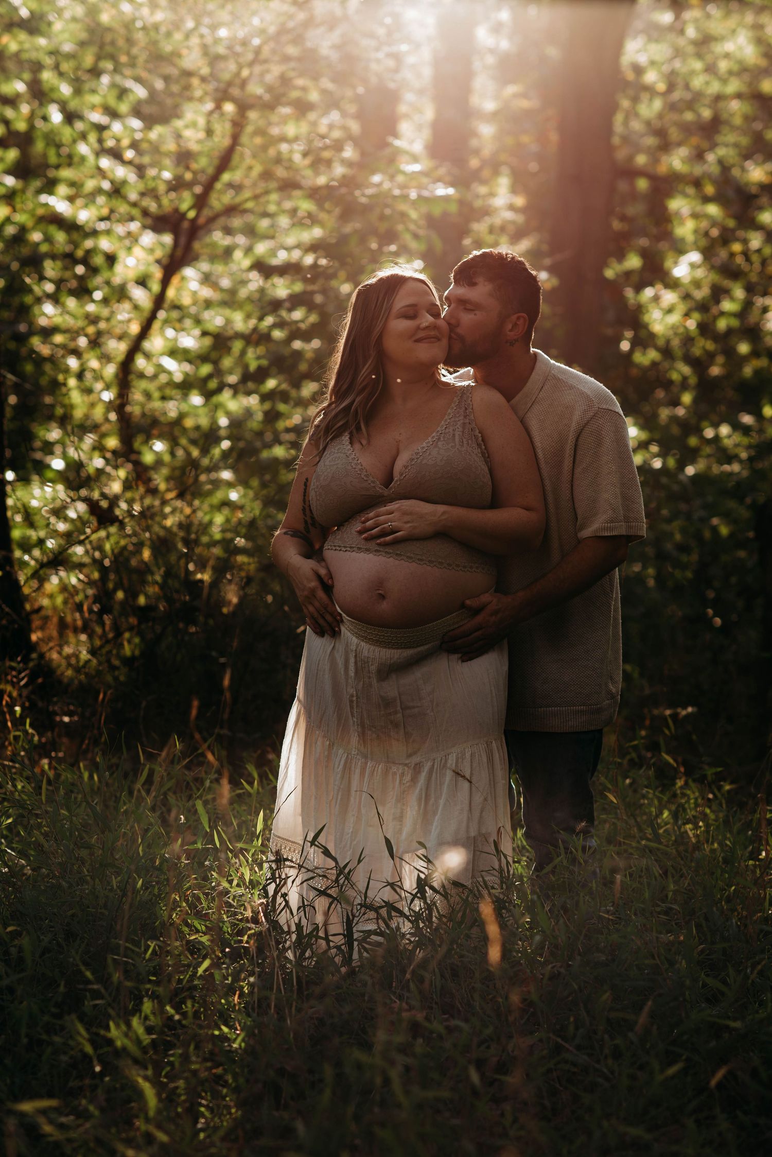 A couple shares an intimate moment in a sunlit meadow during golden hour.