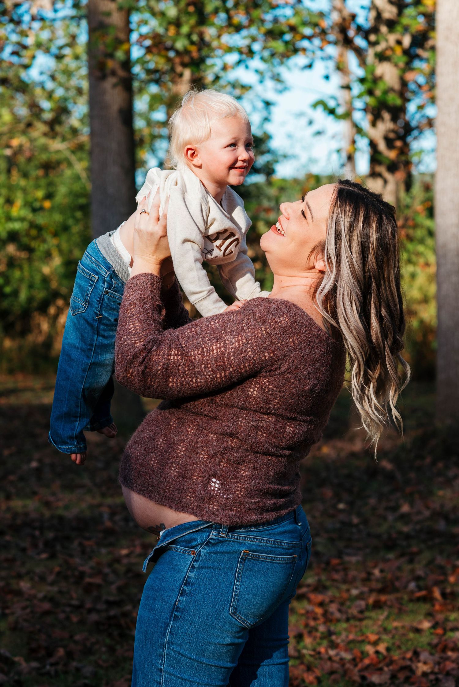 A parent and child share a joyful moment playing together in a wooded autumn setting.