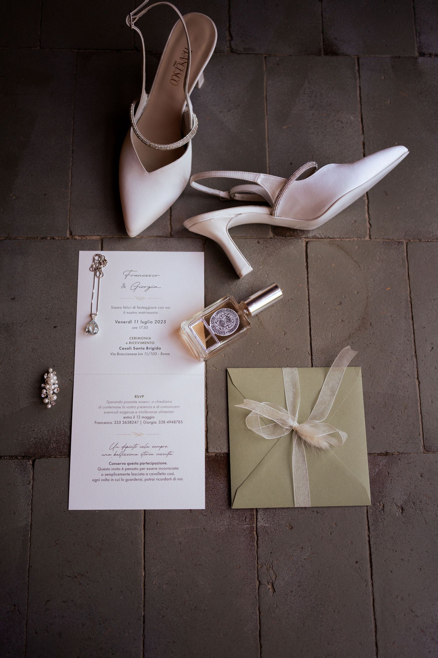 Wedding invitation and elegant white heels arranged on rustic stone floor with delicate ribbon details.