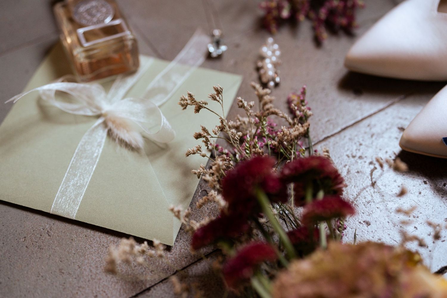 Wedding stationery with burgundy flowers and cream ribbon displayed on textured surface.