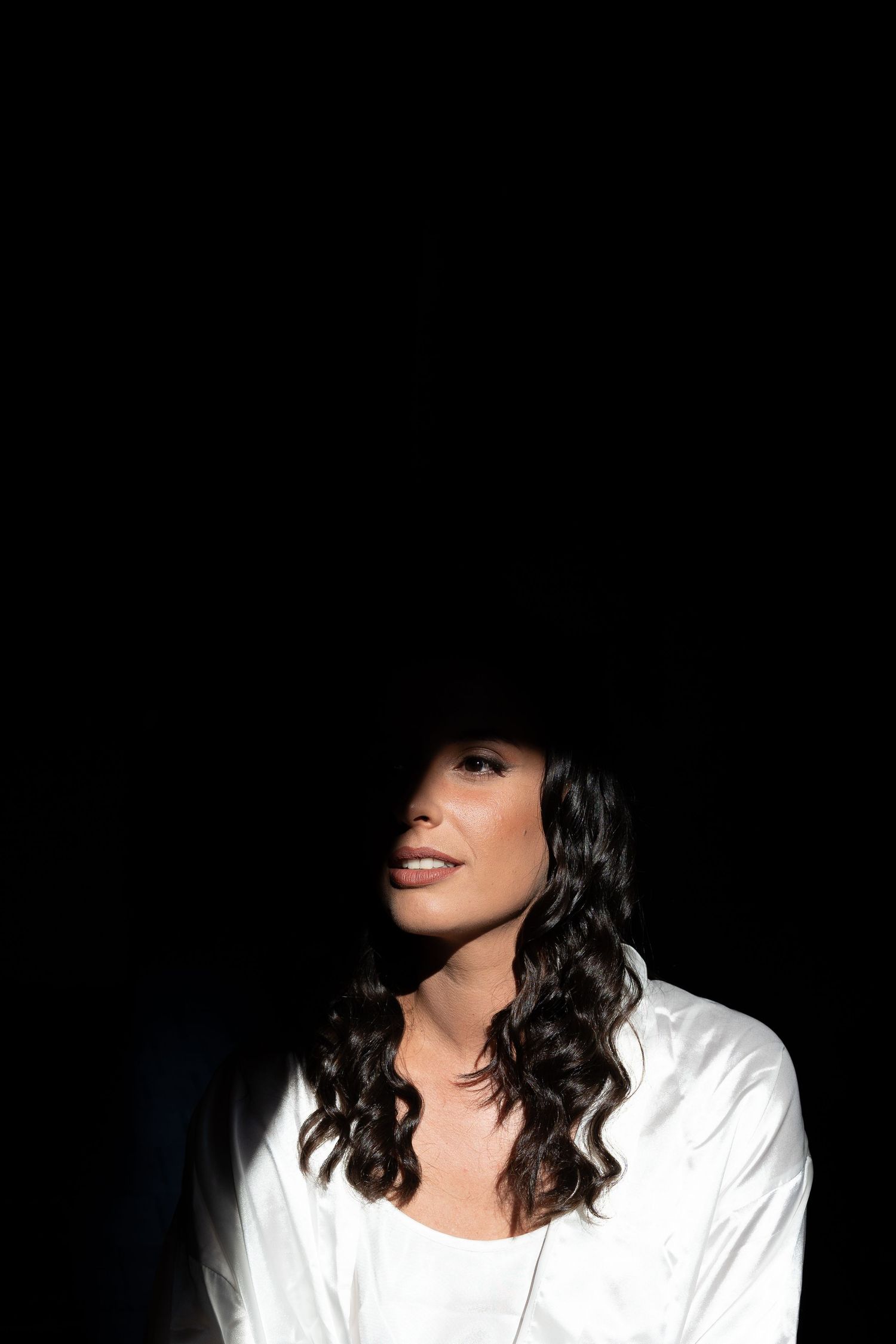 Dramatic portrait against black background showing dark hair and white shirt with upward gaze.