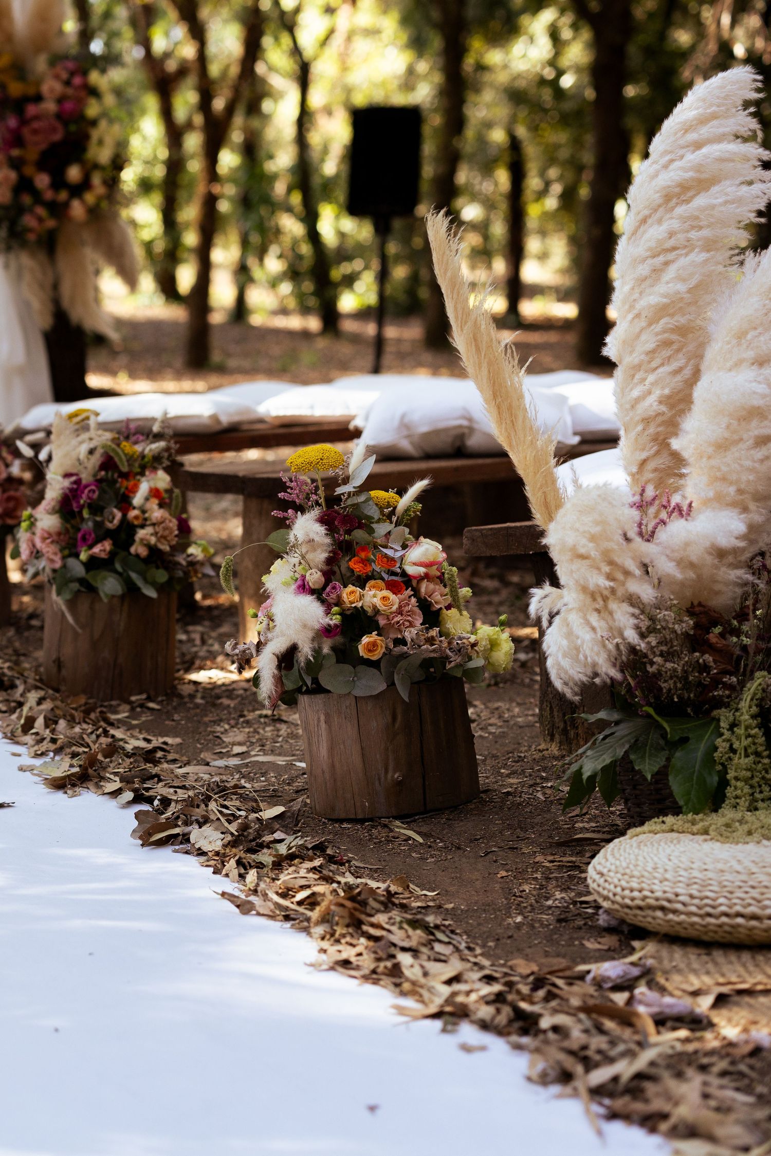 Rustic wooden barrels decorated with fresh flowers and white pampas grass create an elegant outdoor setting.
