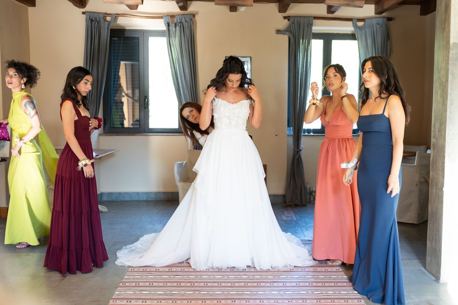 A panoramic view of bridesmaids in colorful dresses standing in a line with a bride in a white wedding gown.