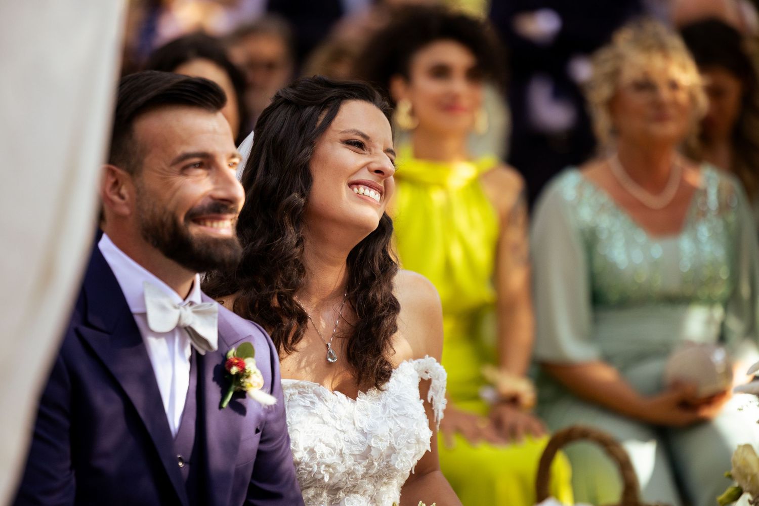 A happy couple shares joyful moments during their outdoor wedding celebration with guests in the background.