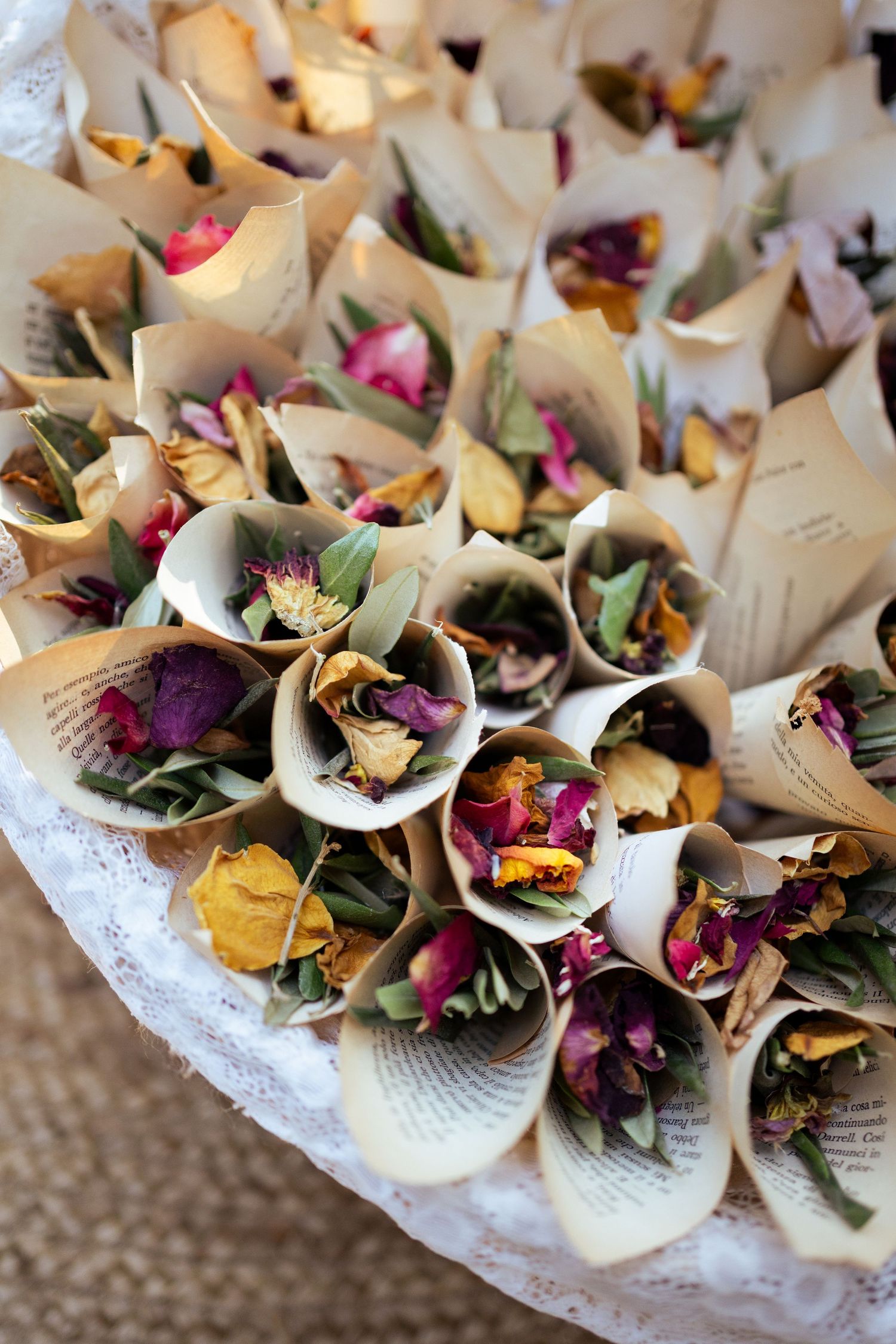Decorative paper cones filled with colorful flower petals arranged on a lace doily.