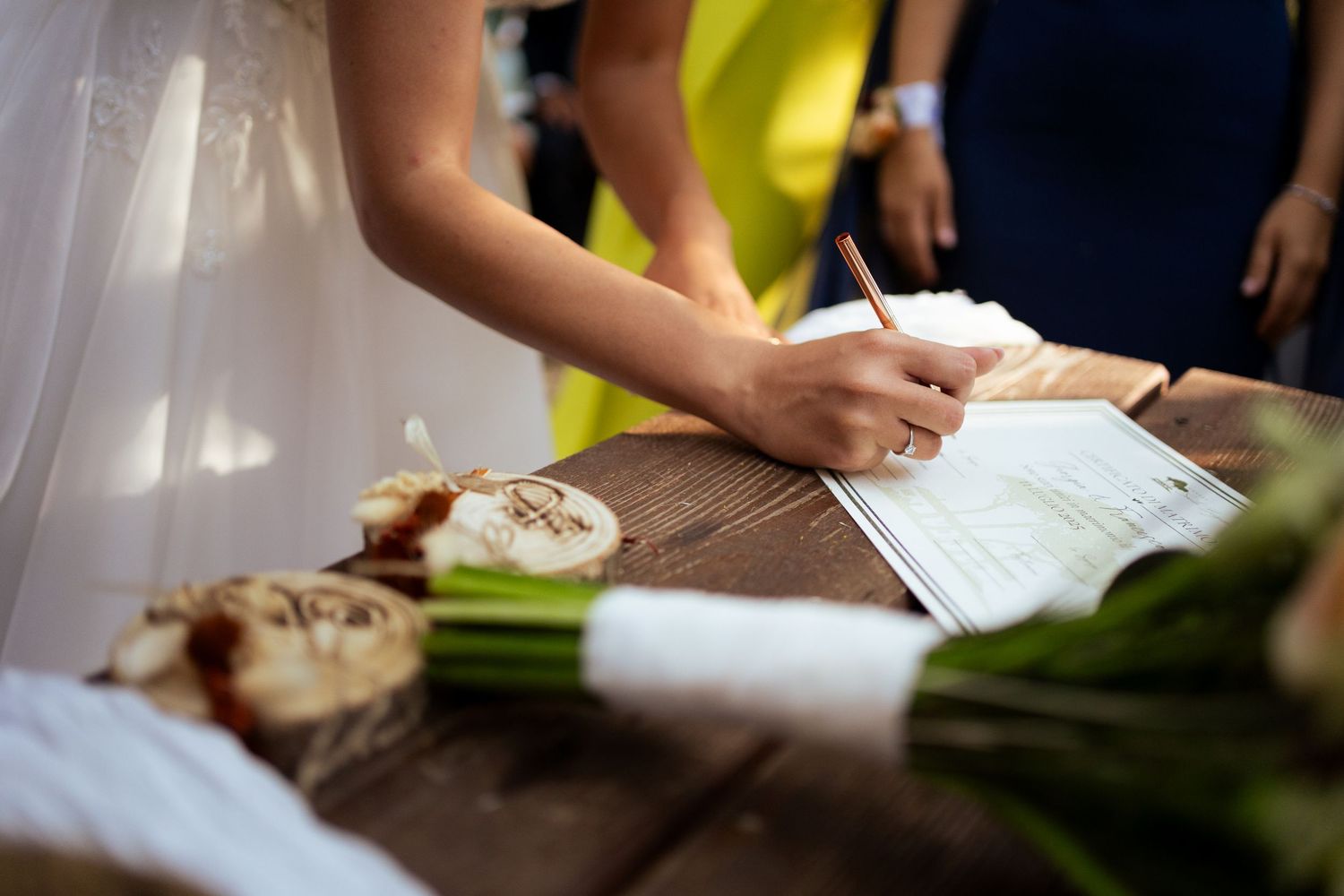 Close-up of hands signing wedding documents at outdoor ceremony.