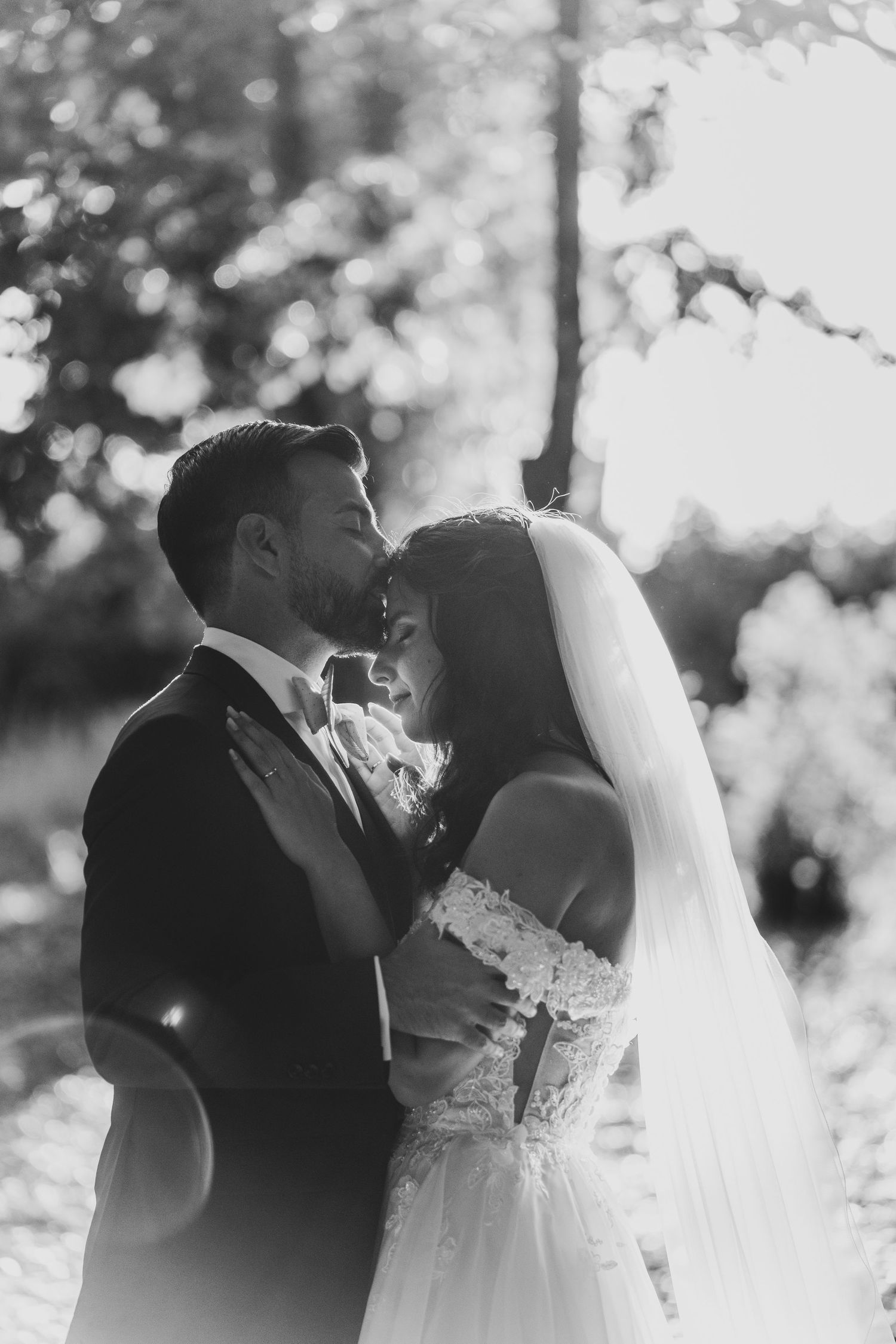 Romantic wedding couple sharing an intimate moment in black and white photography with natural backlighting.