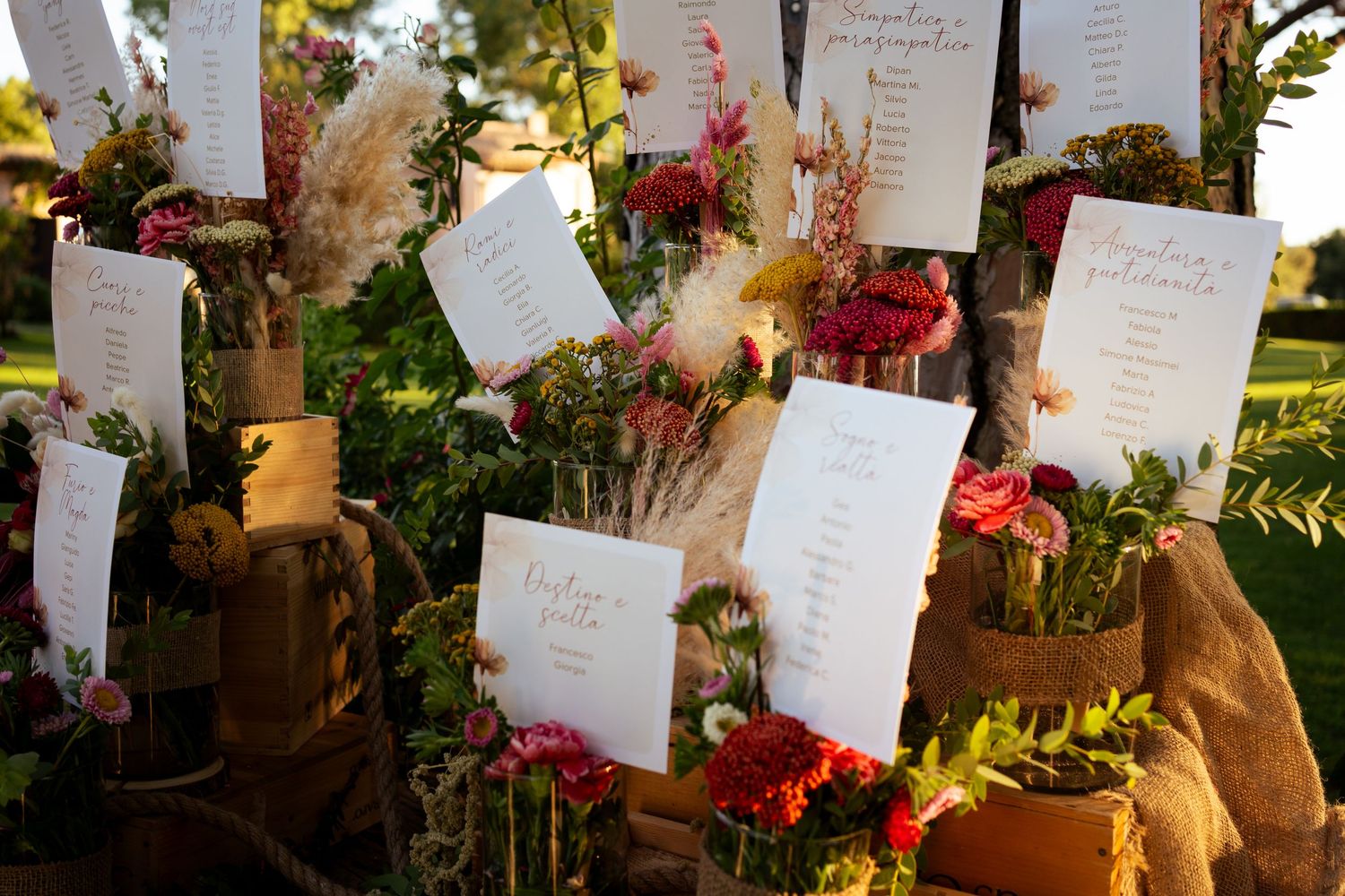 Wedding reception table with floral arrangements and hanging paper seating cards in a rustic outdoor garden setting.