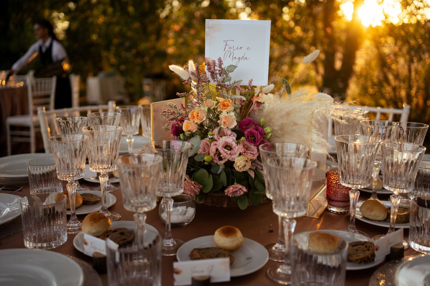 Elegant wedding reception table setting with crystal glasses and floral centerpieces at golden hour.