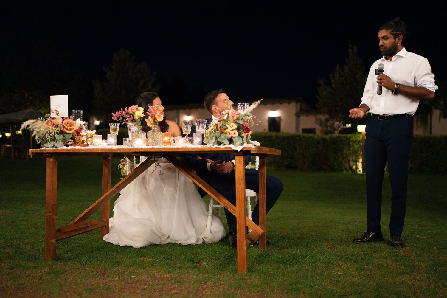 Wedding reception setup with rustic wooden tables outdoors at night.