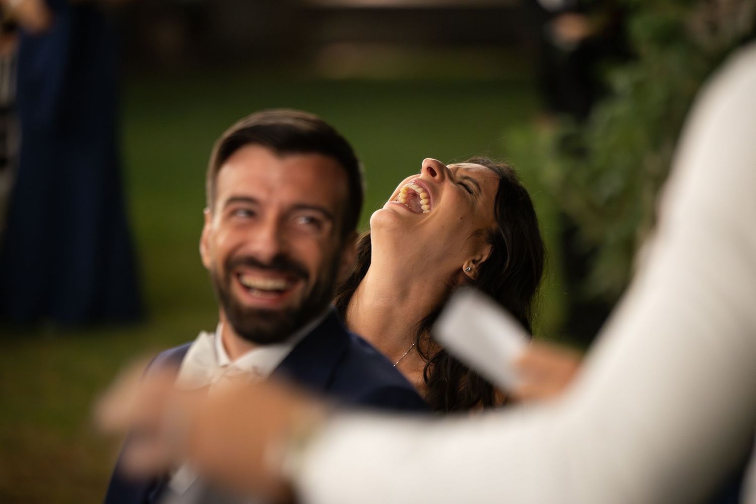 A close-up photo of a smiling person looking upward with blurred greenery in the background.