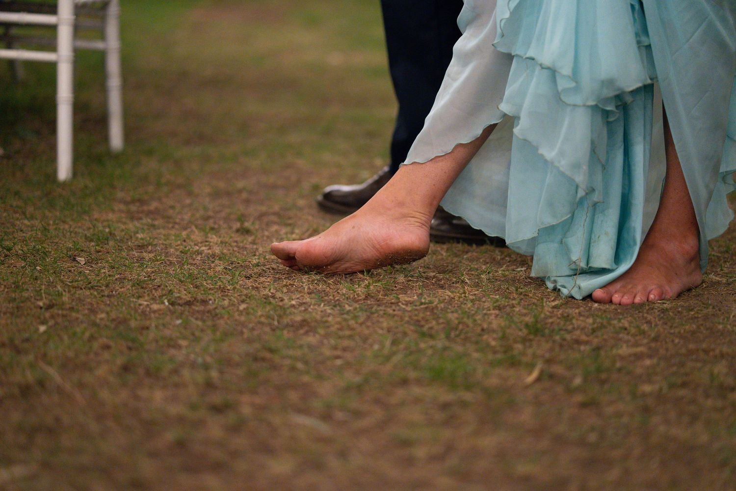 Barefoot person wearing a light blue flowy dress walking on grass at an outdoor event.