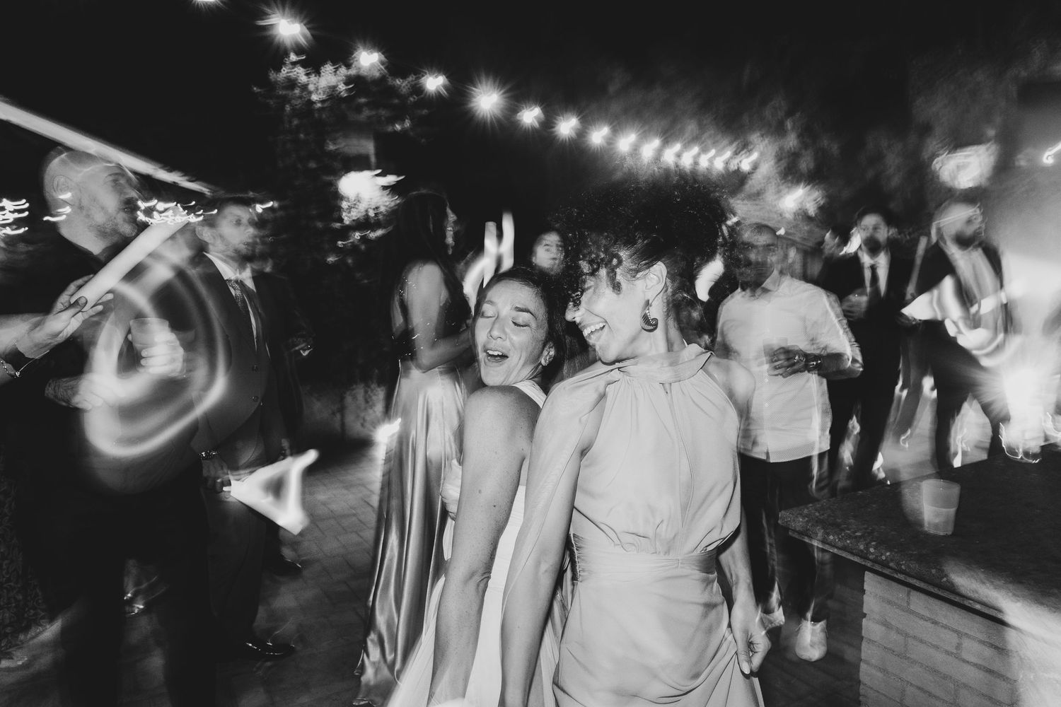 Black and white photo sequence showing people dancing and celebrating at a lively party under string lights.