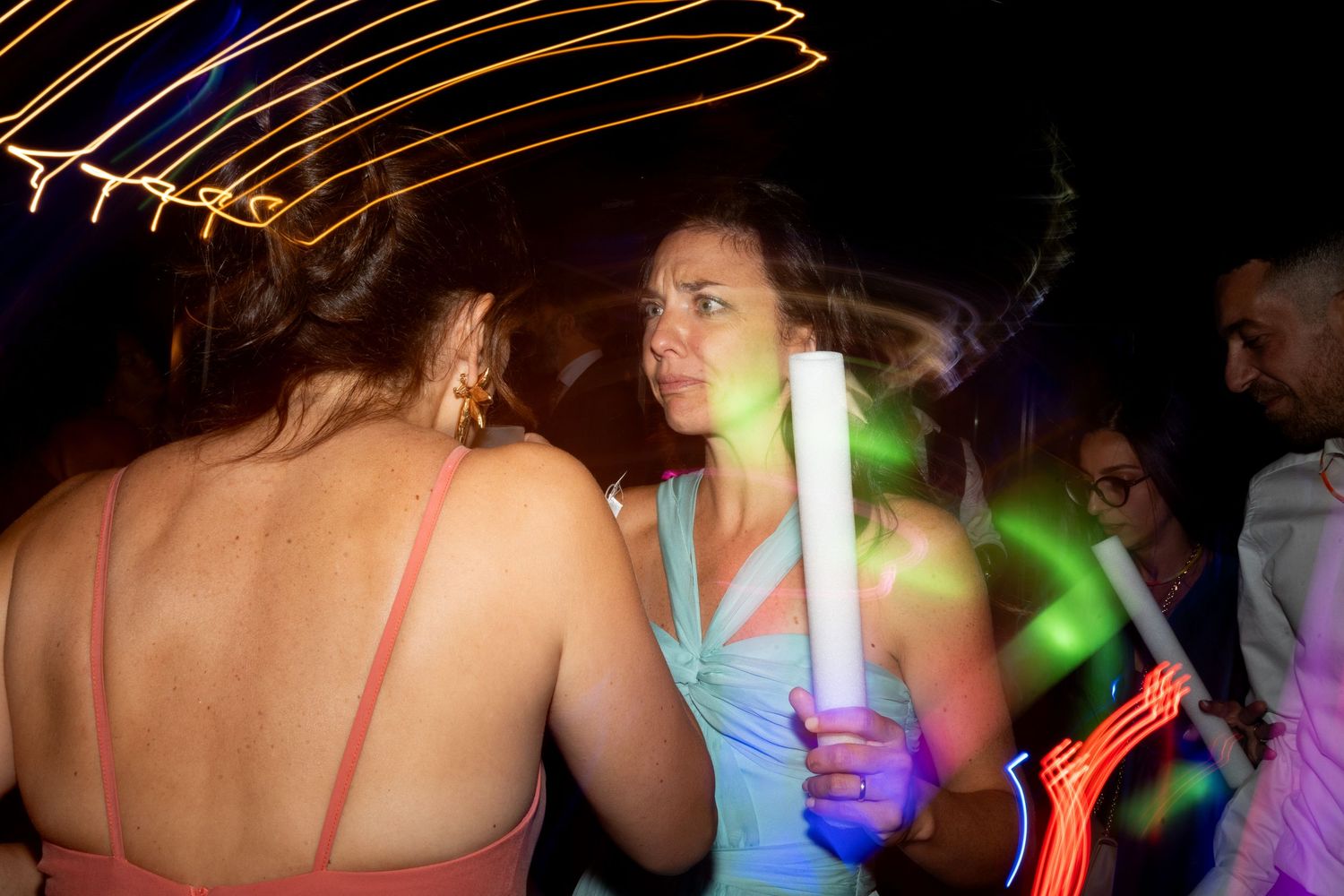 Silhouettes of people dancing with glowing neon light sticks against dark background.