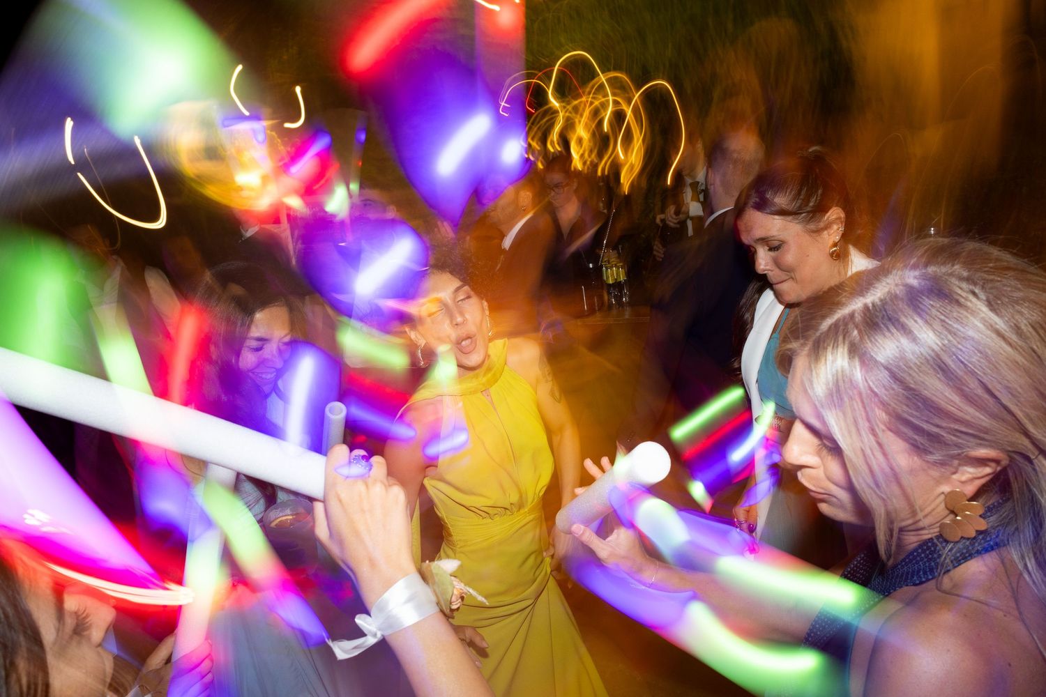 Dancers holding illuminated glow sticks creating light trails in a dark party atmosphere.