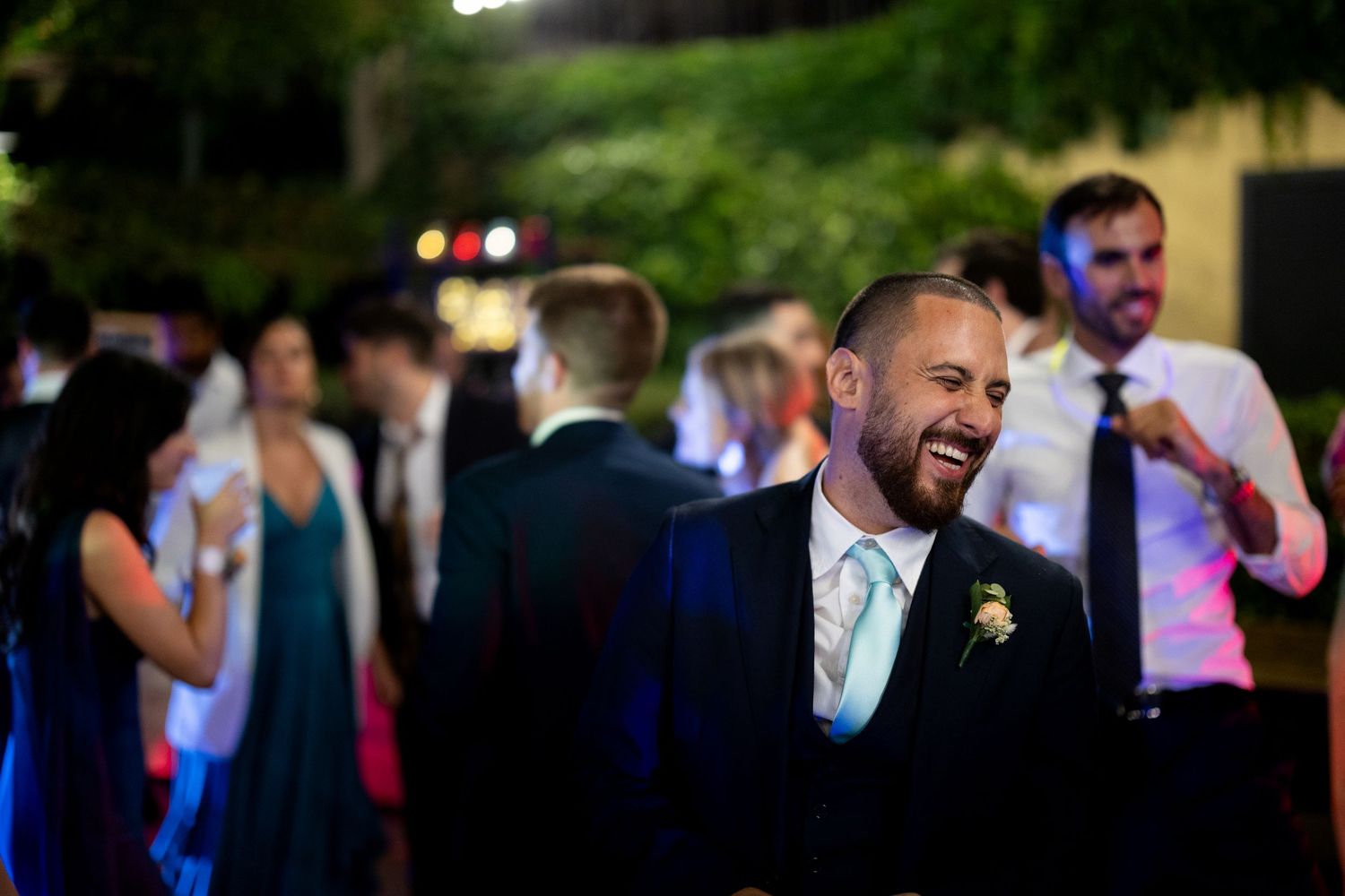 Wedding party members celebrate on a dance floor with colorful lighting and festive atmosphere.