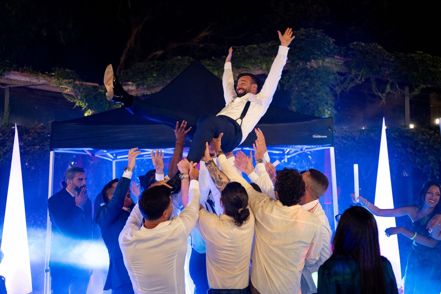 Wedding guests dancing and celebrating on a dark dance floor illuminated by blue lights.