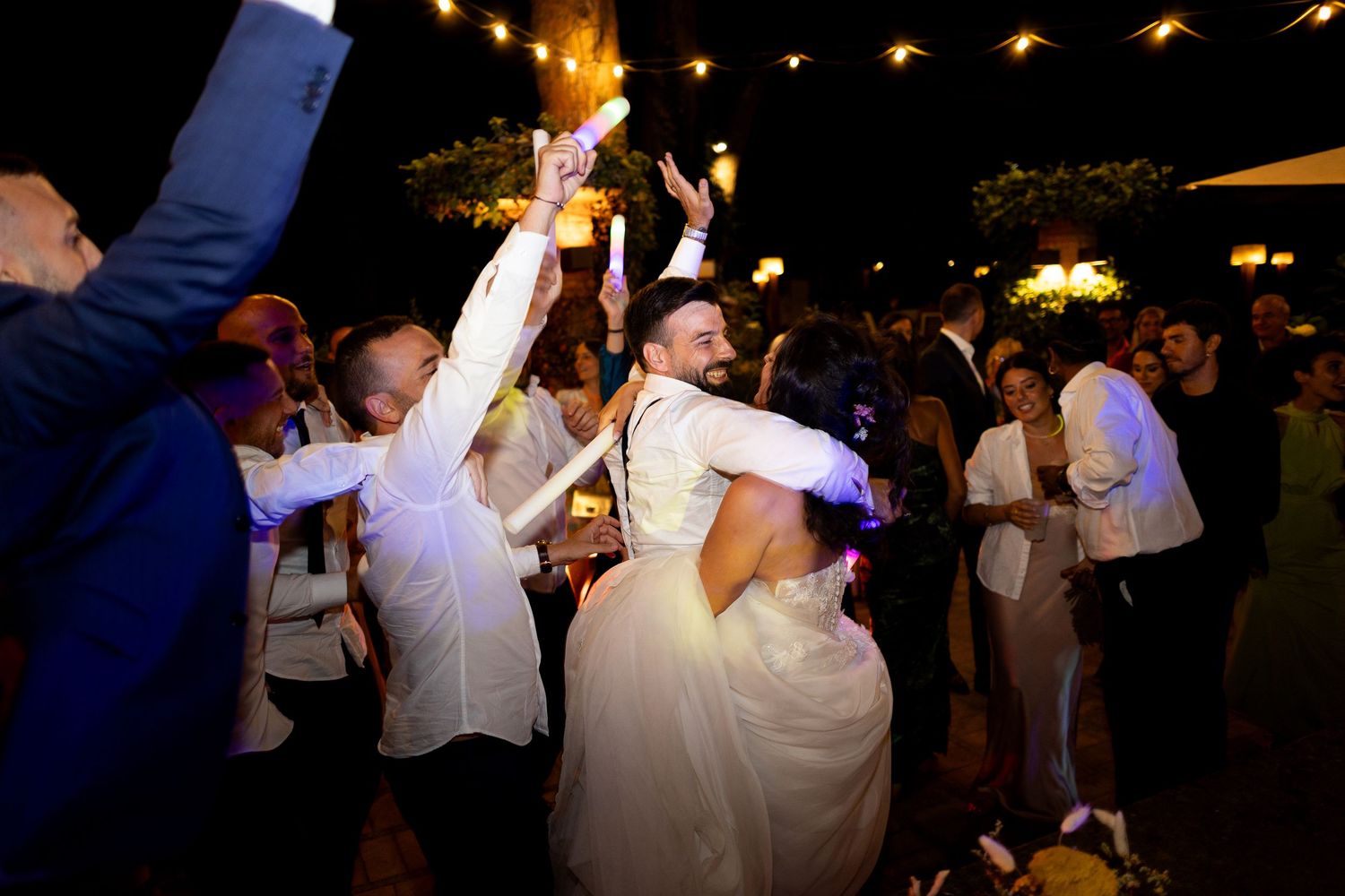 A lively dance party scene with guests dancing under warm lighting at a wedding reception.