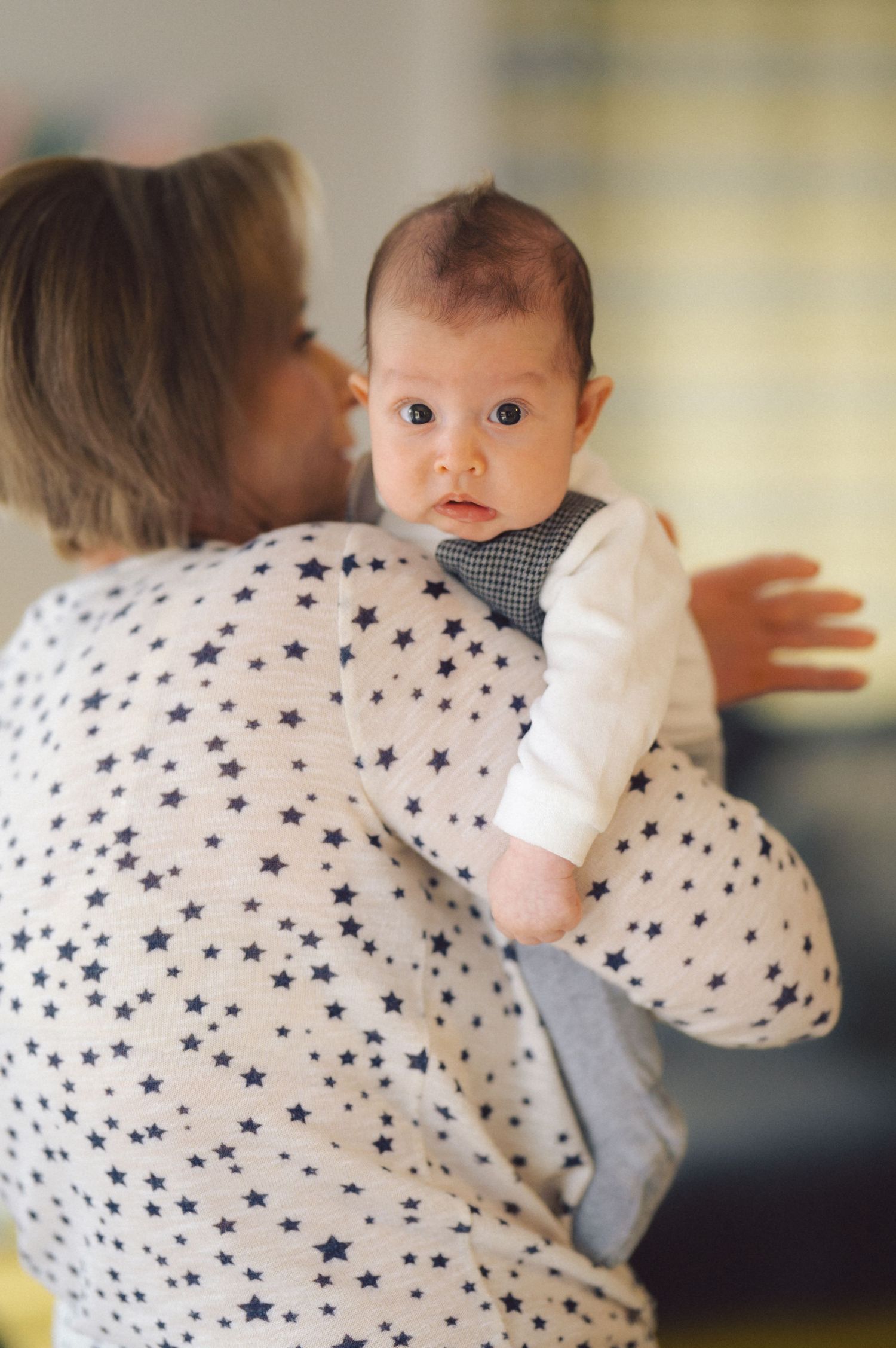 Baby wearing star-printed clothing being held against a soft yellow background.