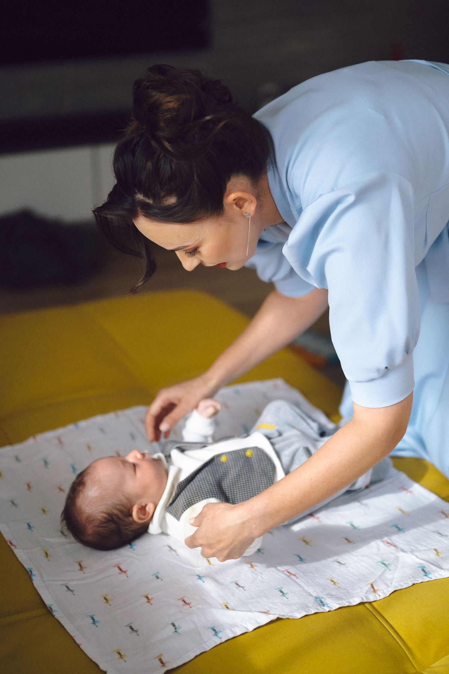 Caregiver in light blue uniform tending to infant on yellow changing surface.