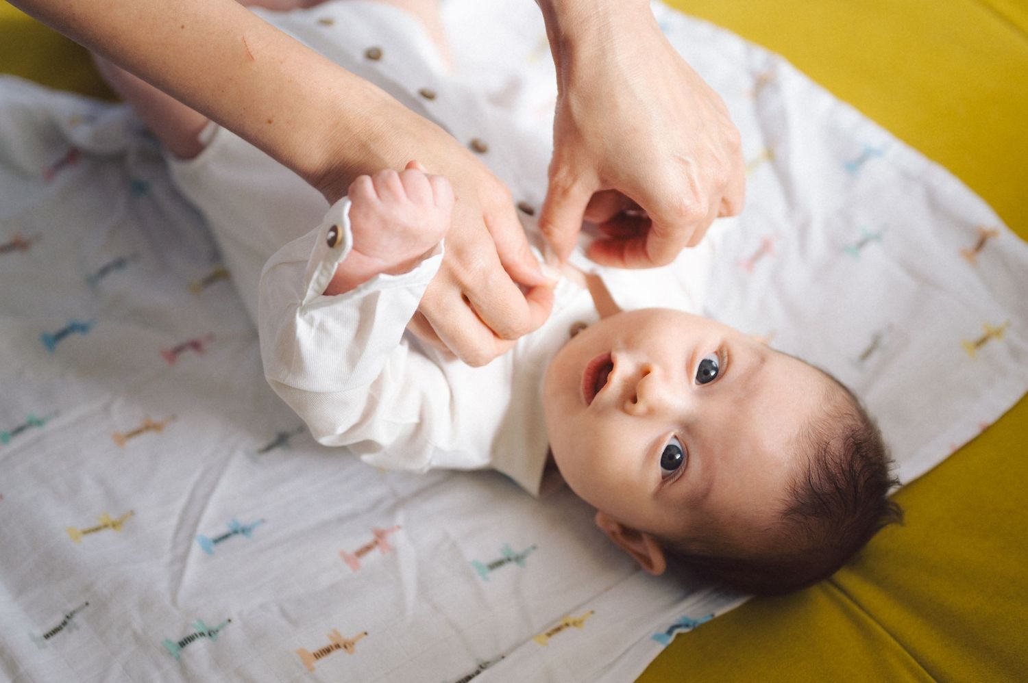 A baby lying on a patterned blanket while hands gently change their clothing.