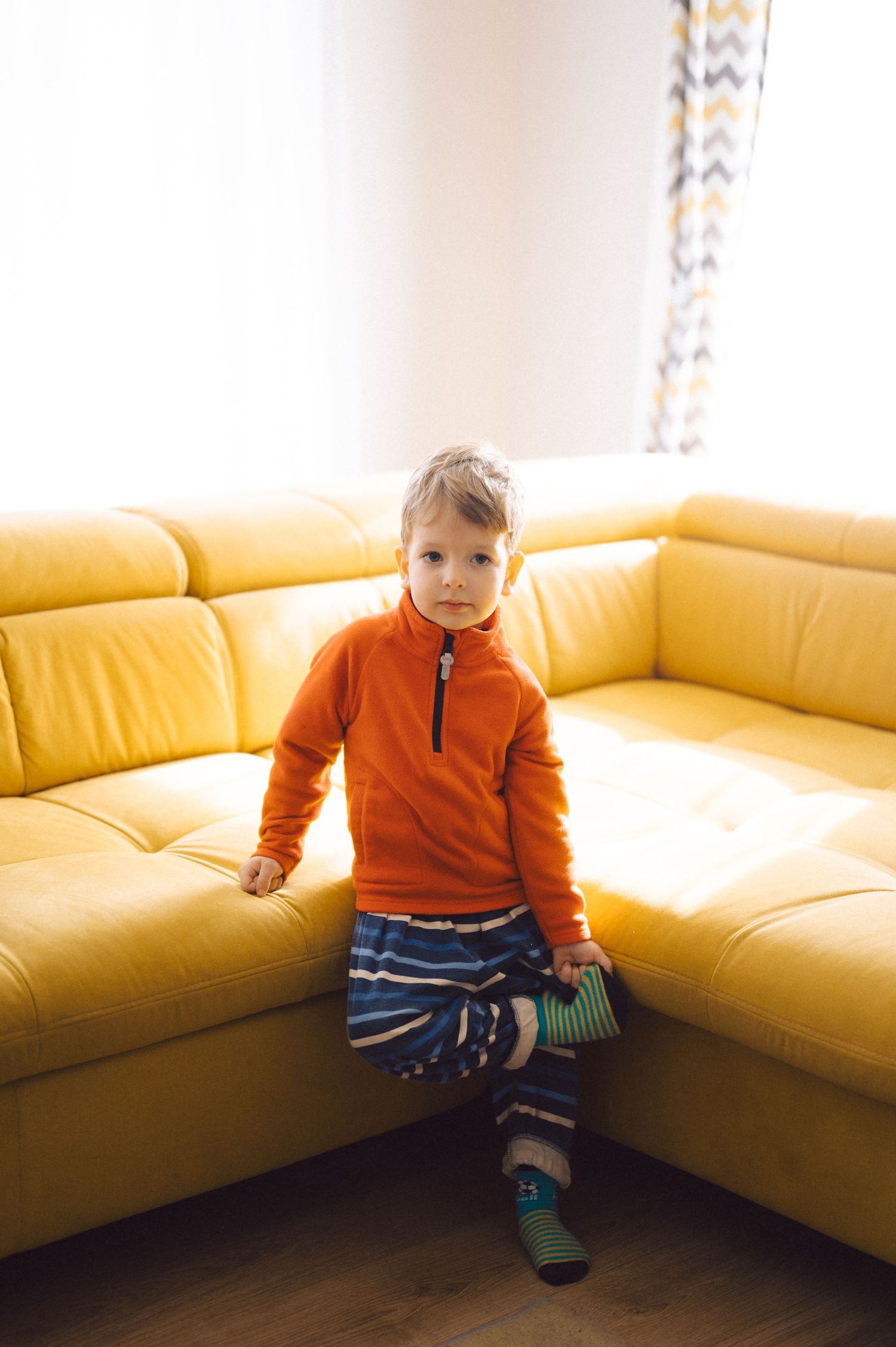A child in an orange sweater sitting on a yellow sectional couch.