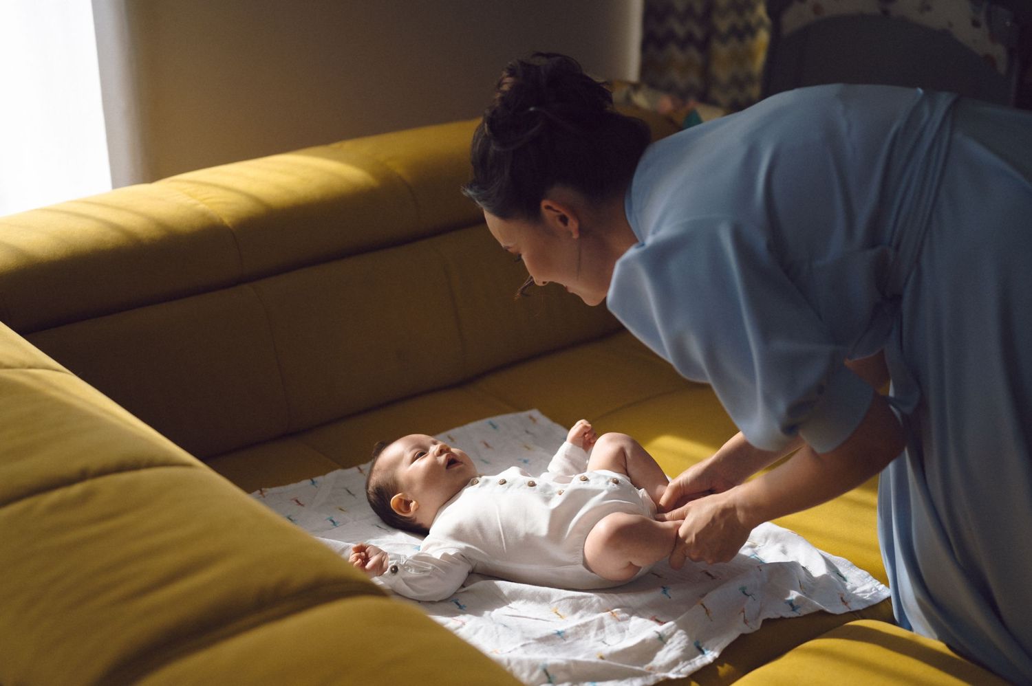 A caregiver changing a baby's clothes on a yellow couch.