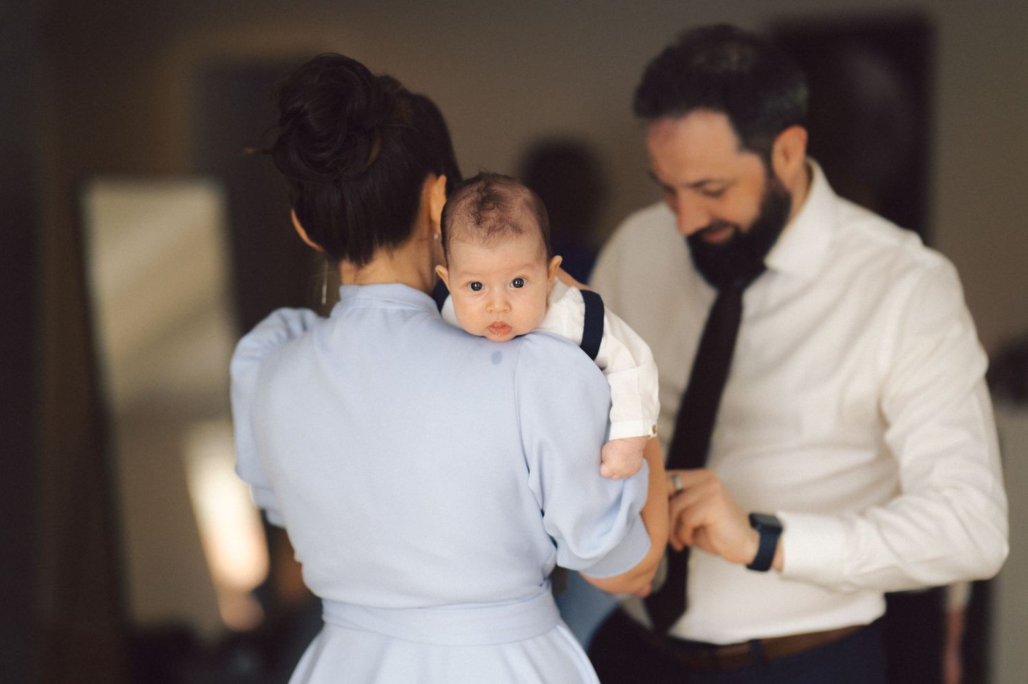 A couple holding their baby while standing together in a dimly lit room.