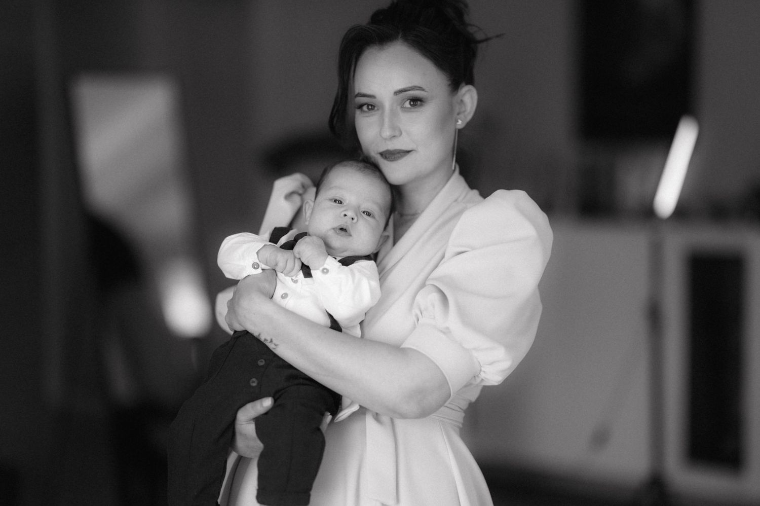A parent in white clothing holding a baby in a black and white portrait.