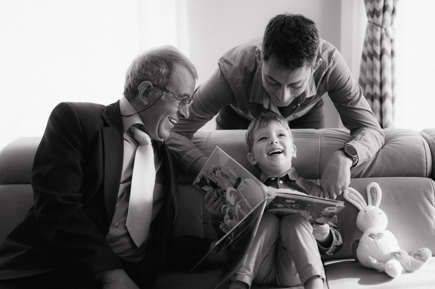 Three generations share a tender moment while reading together on a couch.